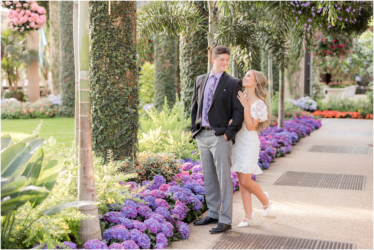 bride stands behind groom hugging him next to purple flowers at Longwood Gardens