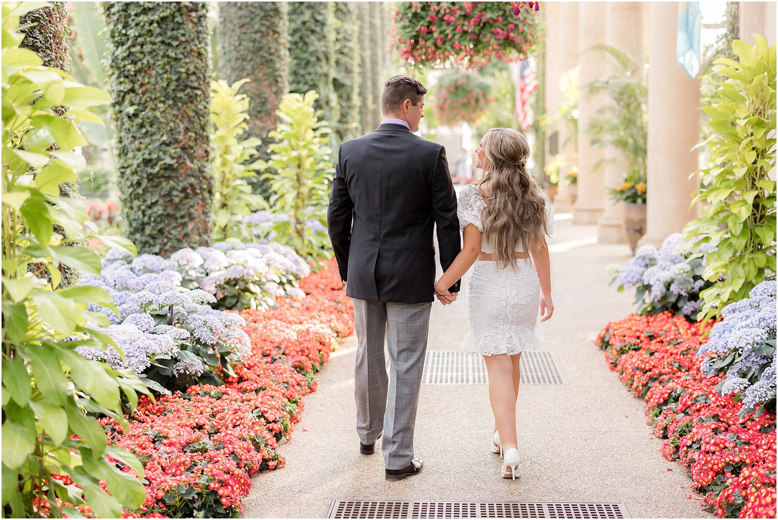 bride and groom hold hands walking between flowers at Longwood Gardens