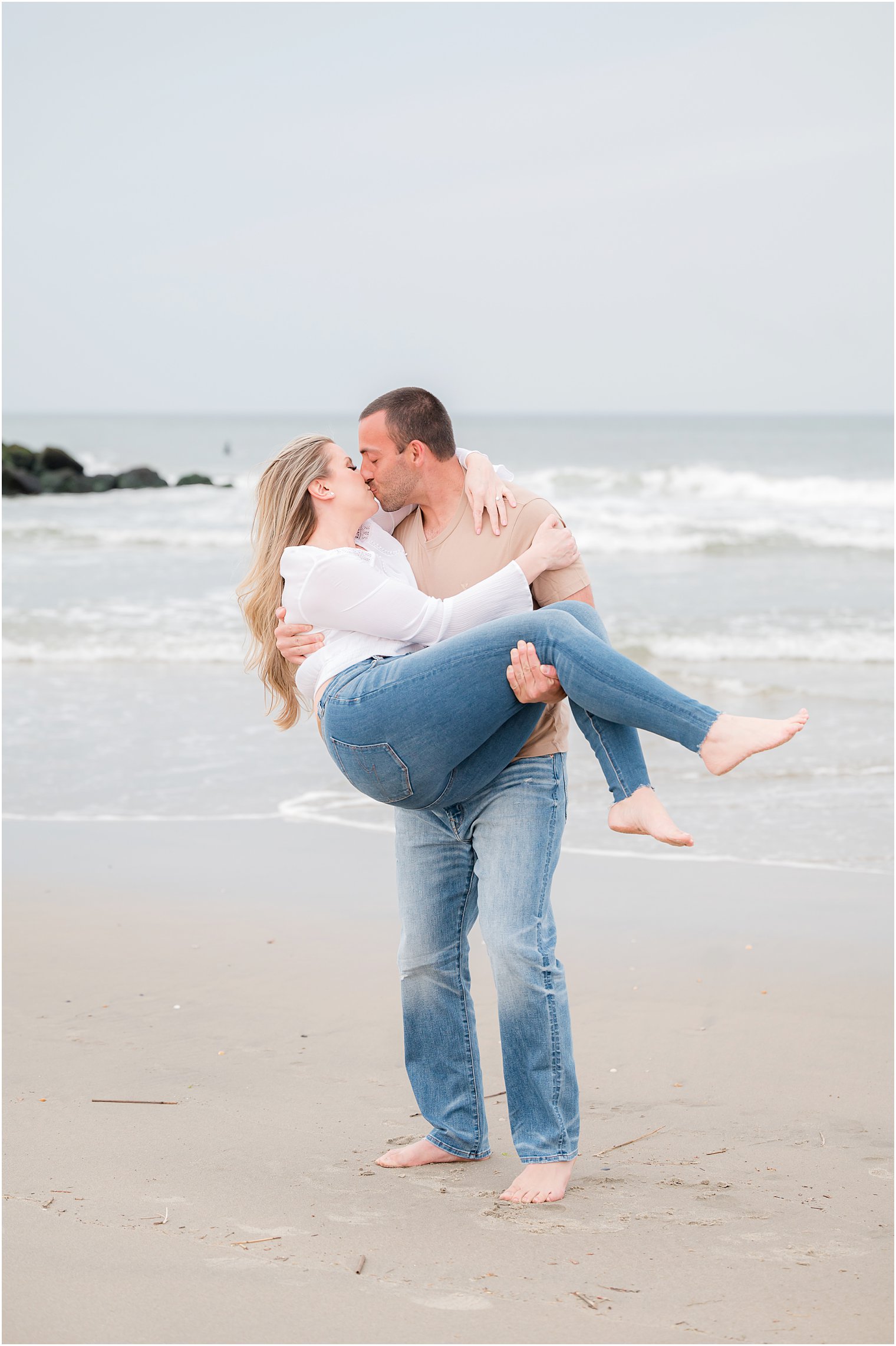 man lifts up woman on beach kissing her during Spring Lake engagement session