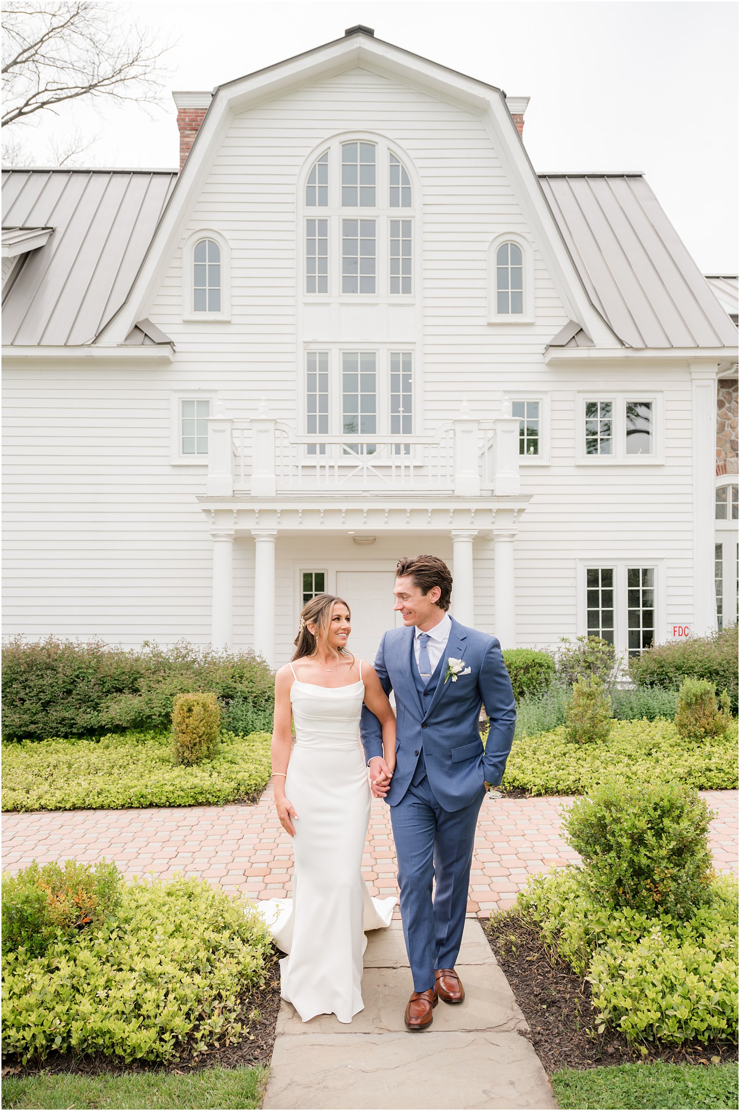 newlyweds hold hands walking in front of barn at Ryland Inn