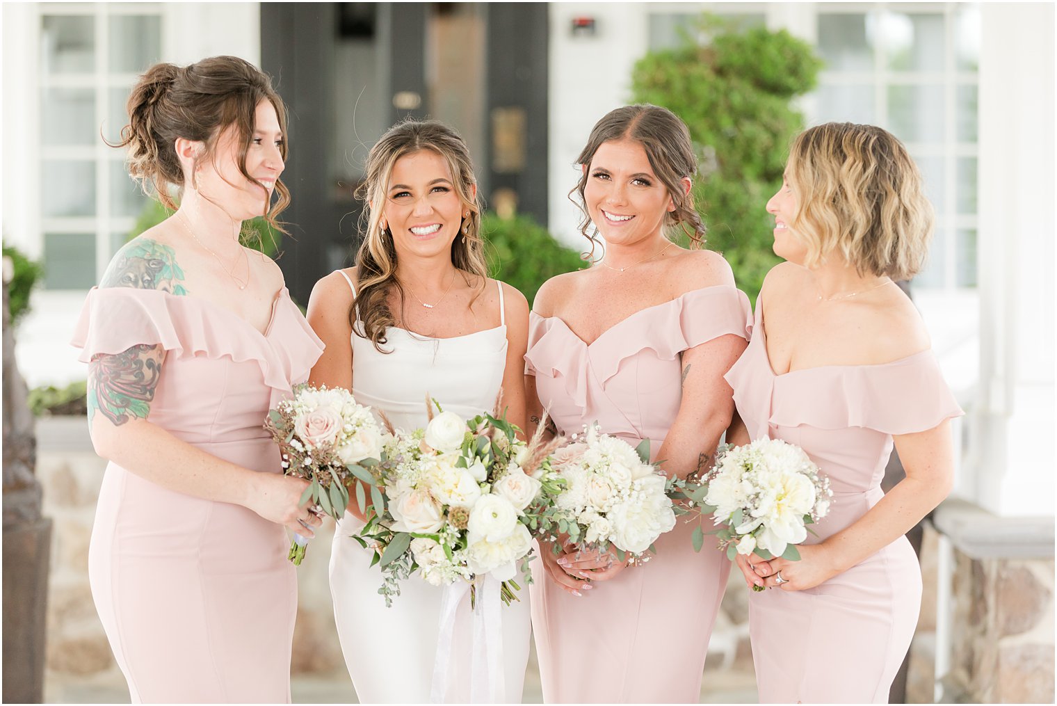 bridesmaids in pink dresses hold white bouquets smiling with bride
