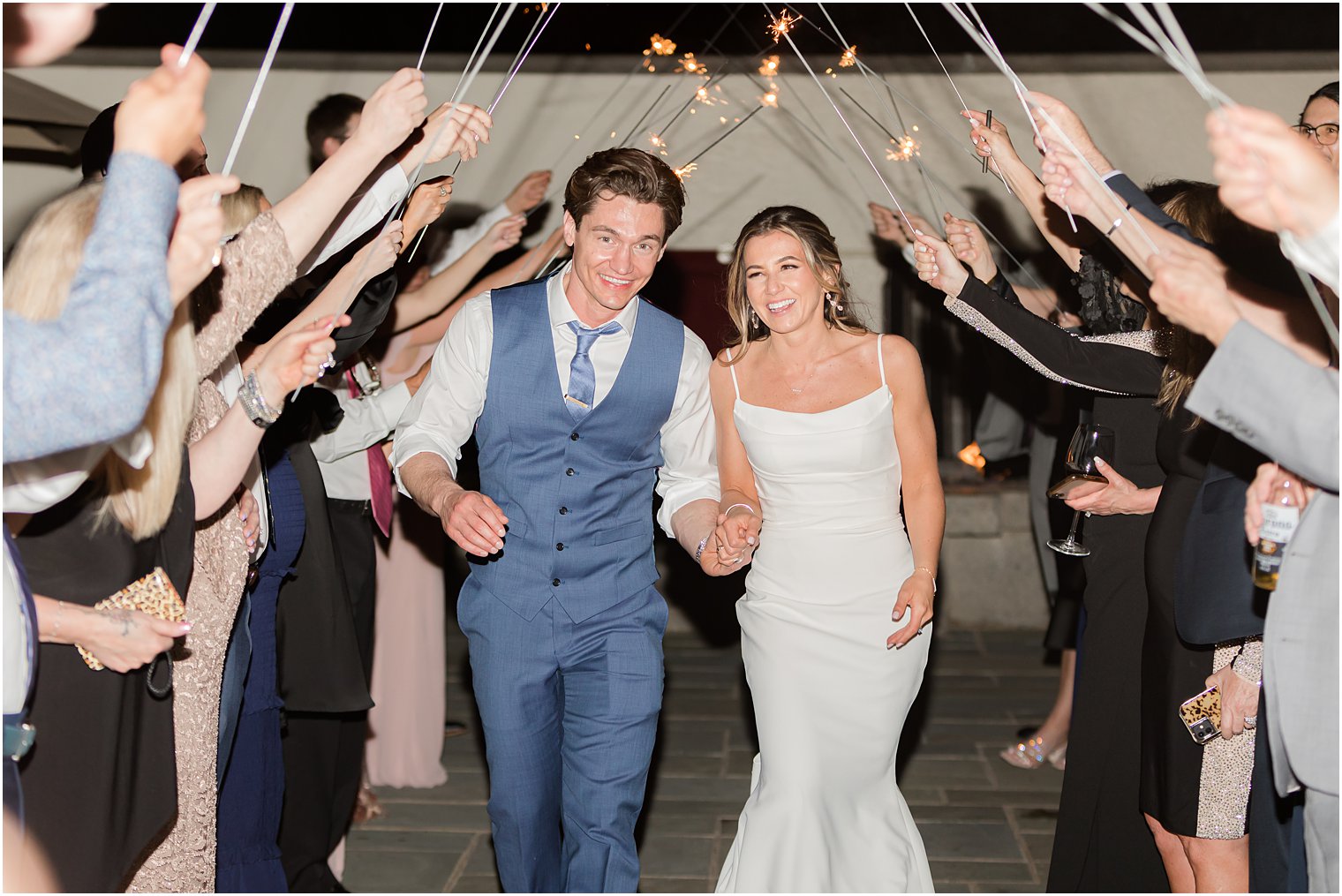 newlyweds hold hands going under sparklers after Ryland Inn wedding reception