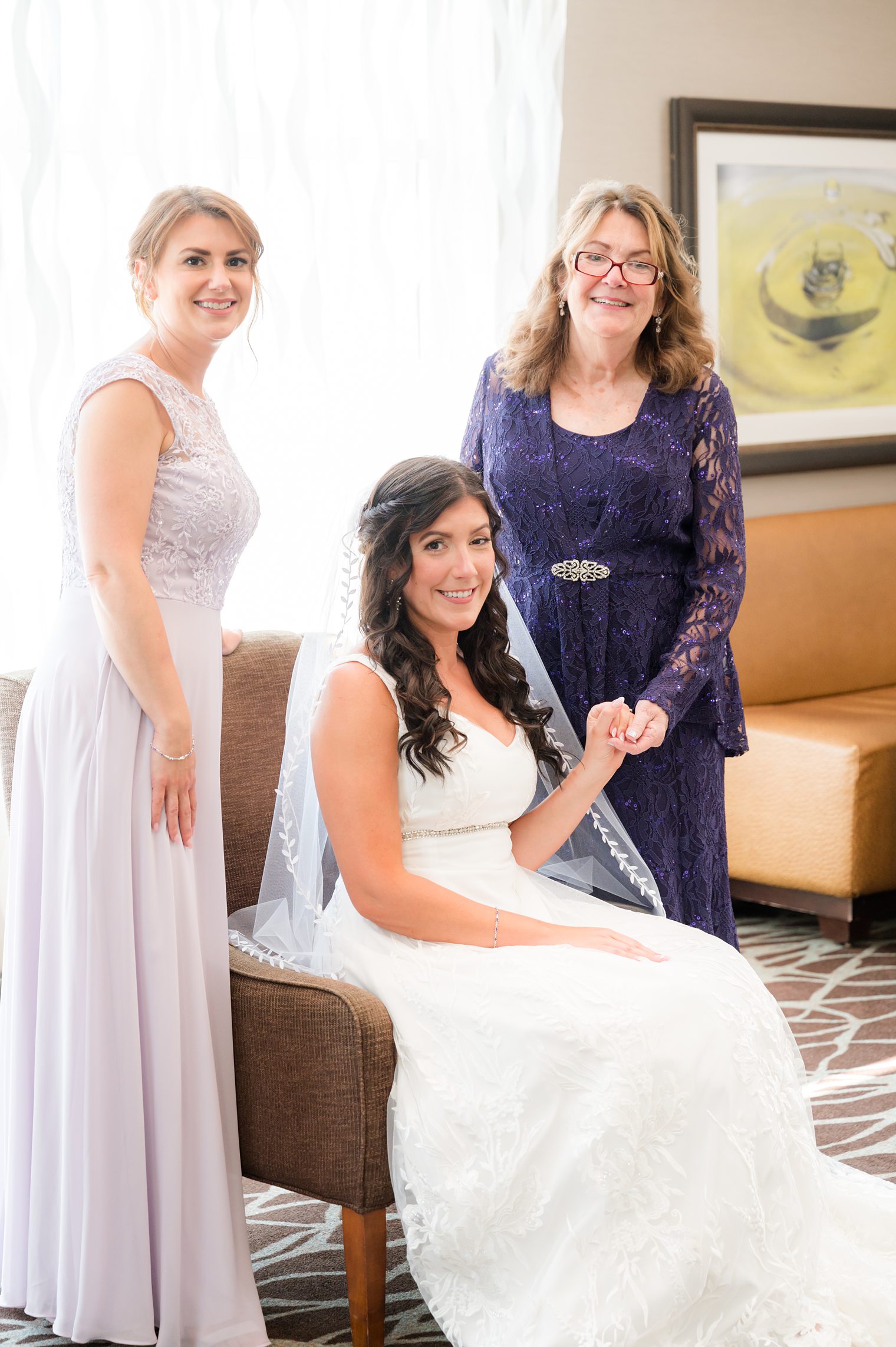 Bride with her mother and sister happily waiting for the big moment at Bride helped by her sister to get ready to say I do at Windows on the Water at Frogbridge