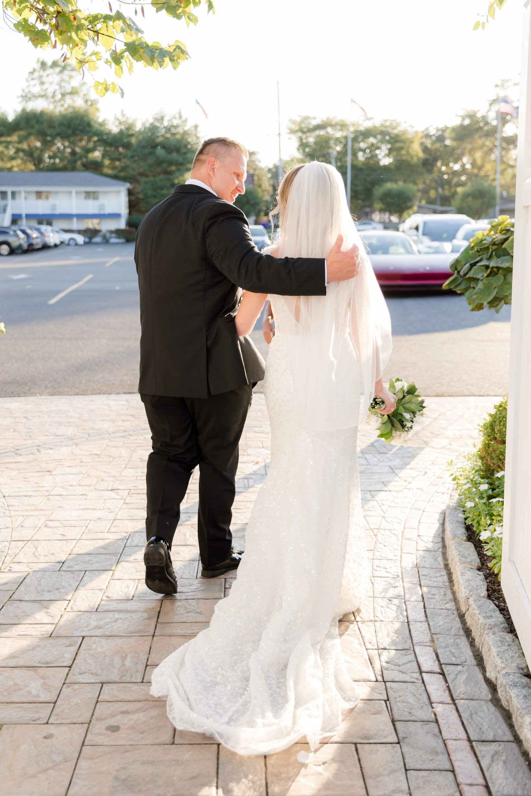 Bride and groom walking away together after the ceremony, with the groom’s arm around the bride’s back as they walk along a paved path in an outdoor setting with greenery