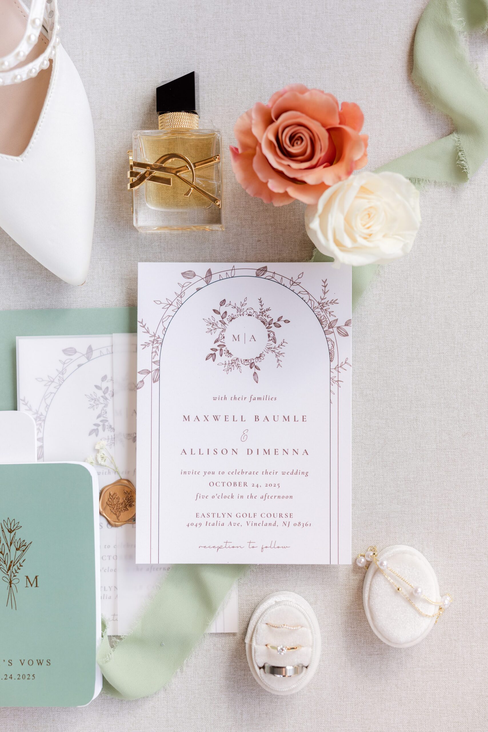 Wedding invitations, rings, and perfume are beautifully arranged with soft florals and silk ribbon, creating a romantic still life that reflects the elegance of the day