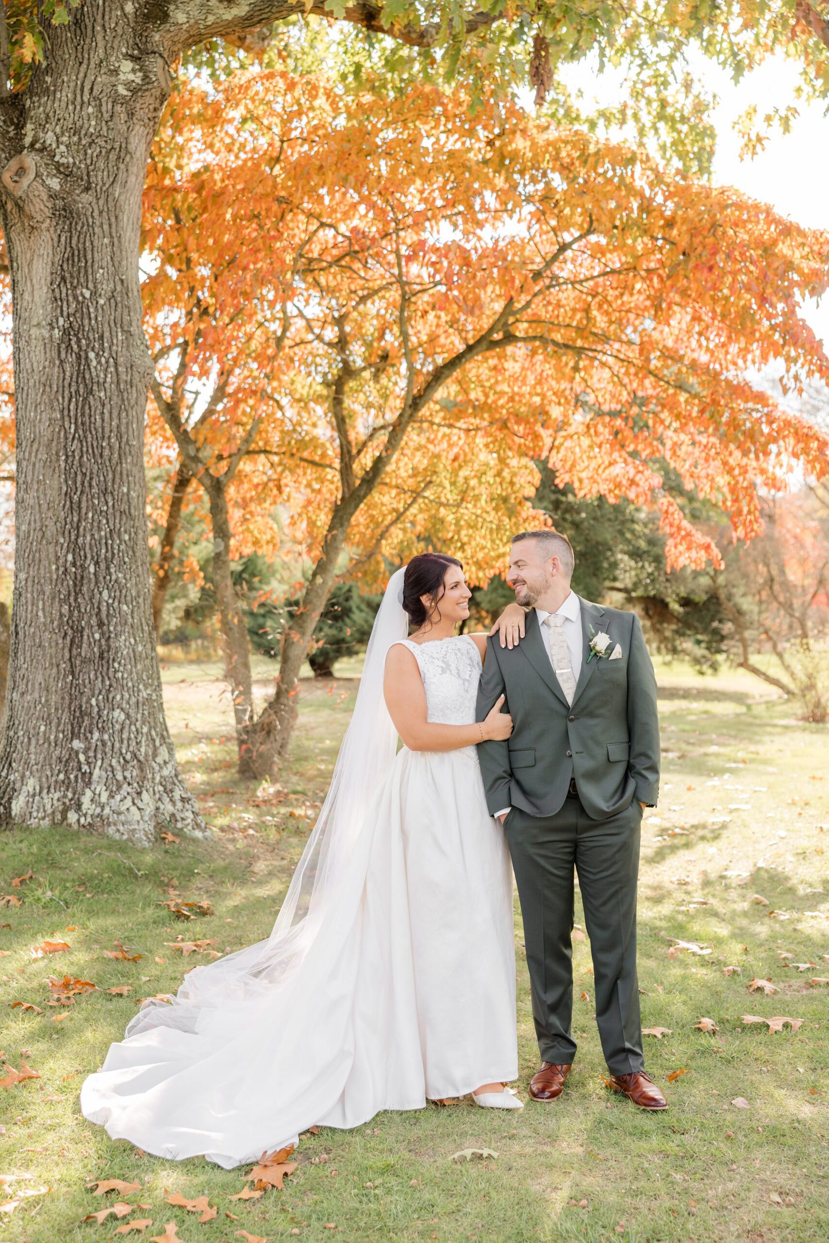 Beneath a canopy of glowing autumn leaves, the couple stands close, lost in each other’s presence