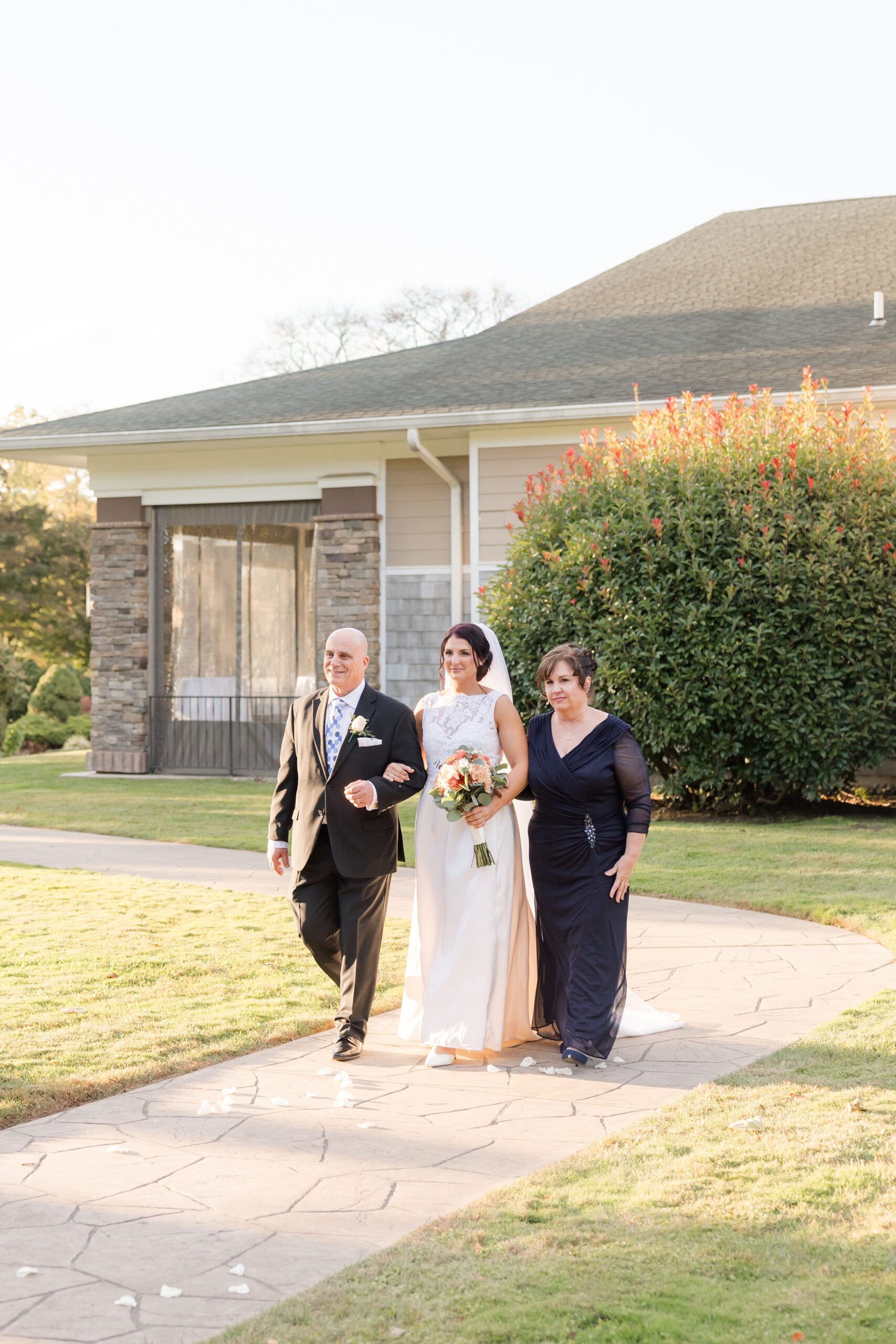 Bride walks down the aisle with her parents, all three smiling with pride and emotion as they share a meaningful moment before the ceremony