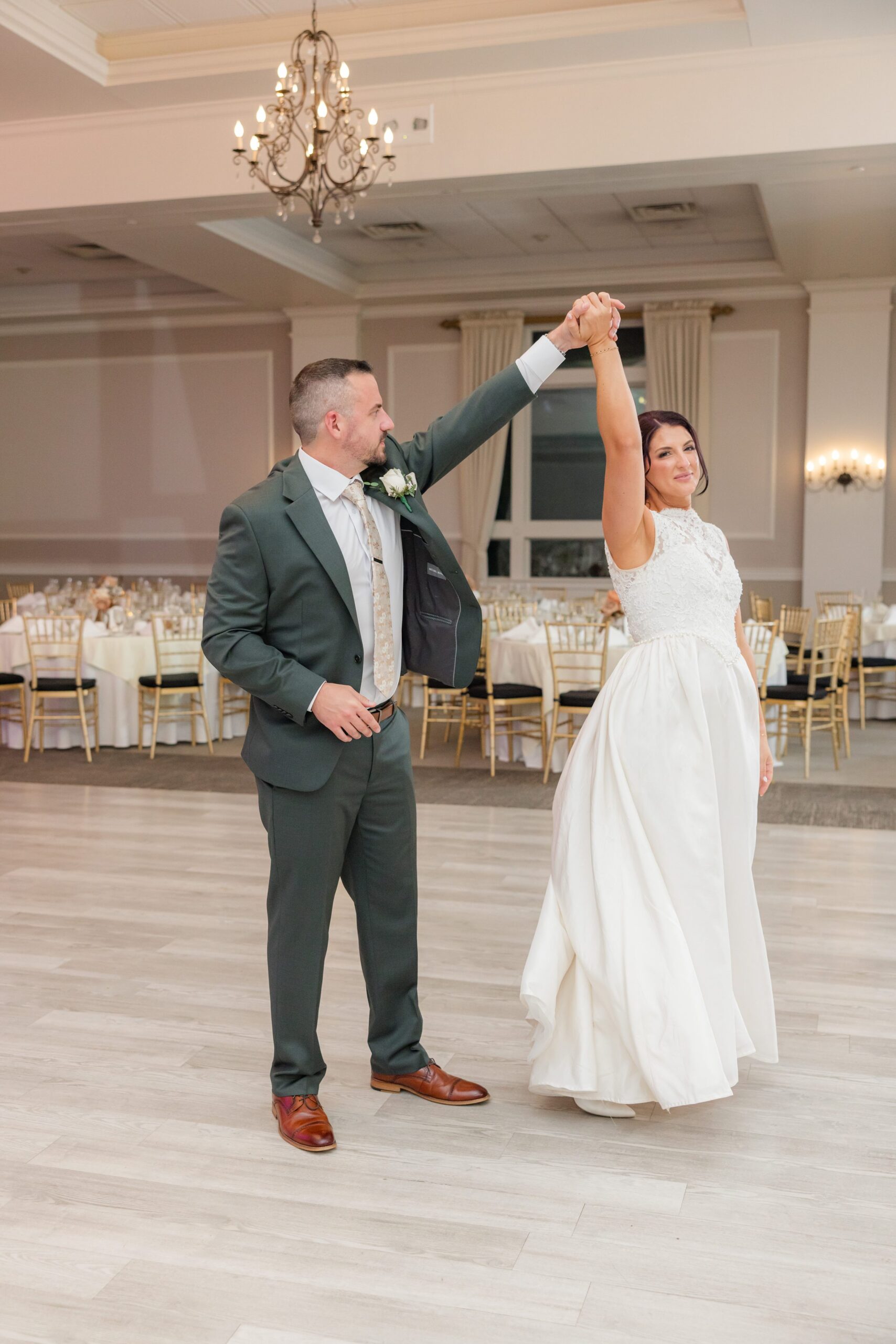 Groom twirls his bride beneath soft lighting, her dress flowing as they dance together