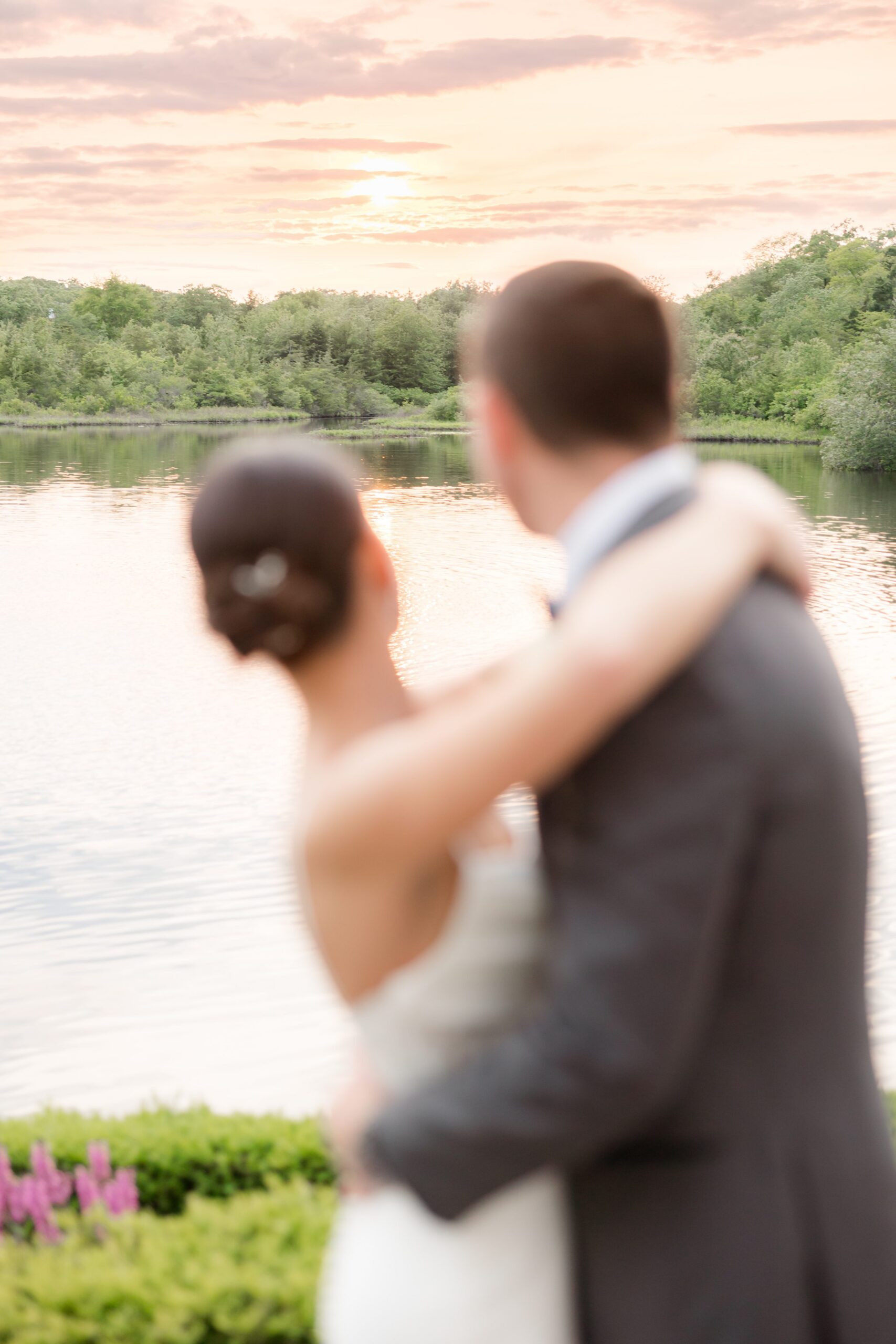 Out-of-focus photo of bride and groom looking out into the lake while holding each other