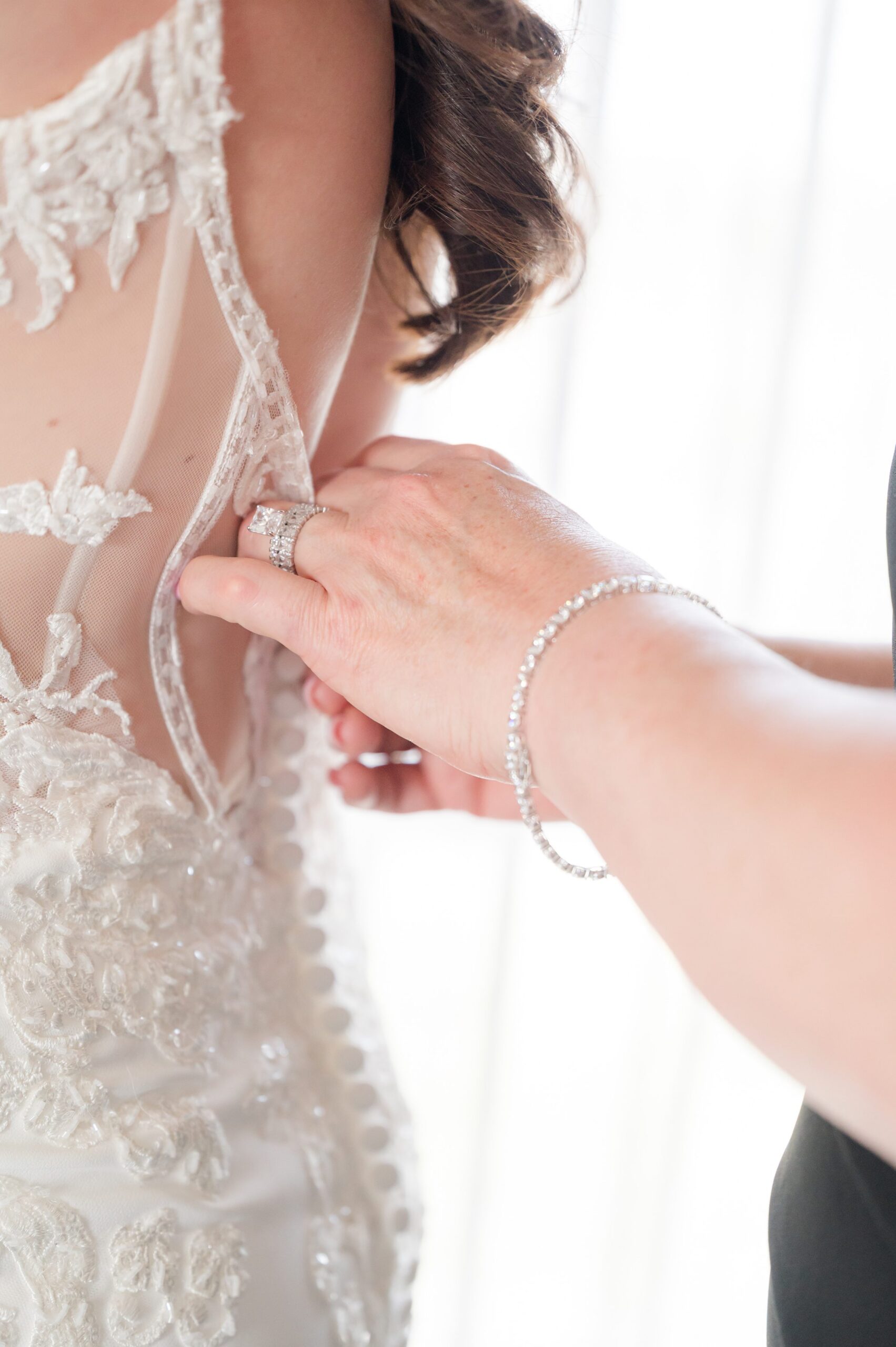 Bride being gently buttoned into her lace wedding gown, capturing a soft moment
