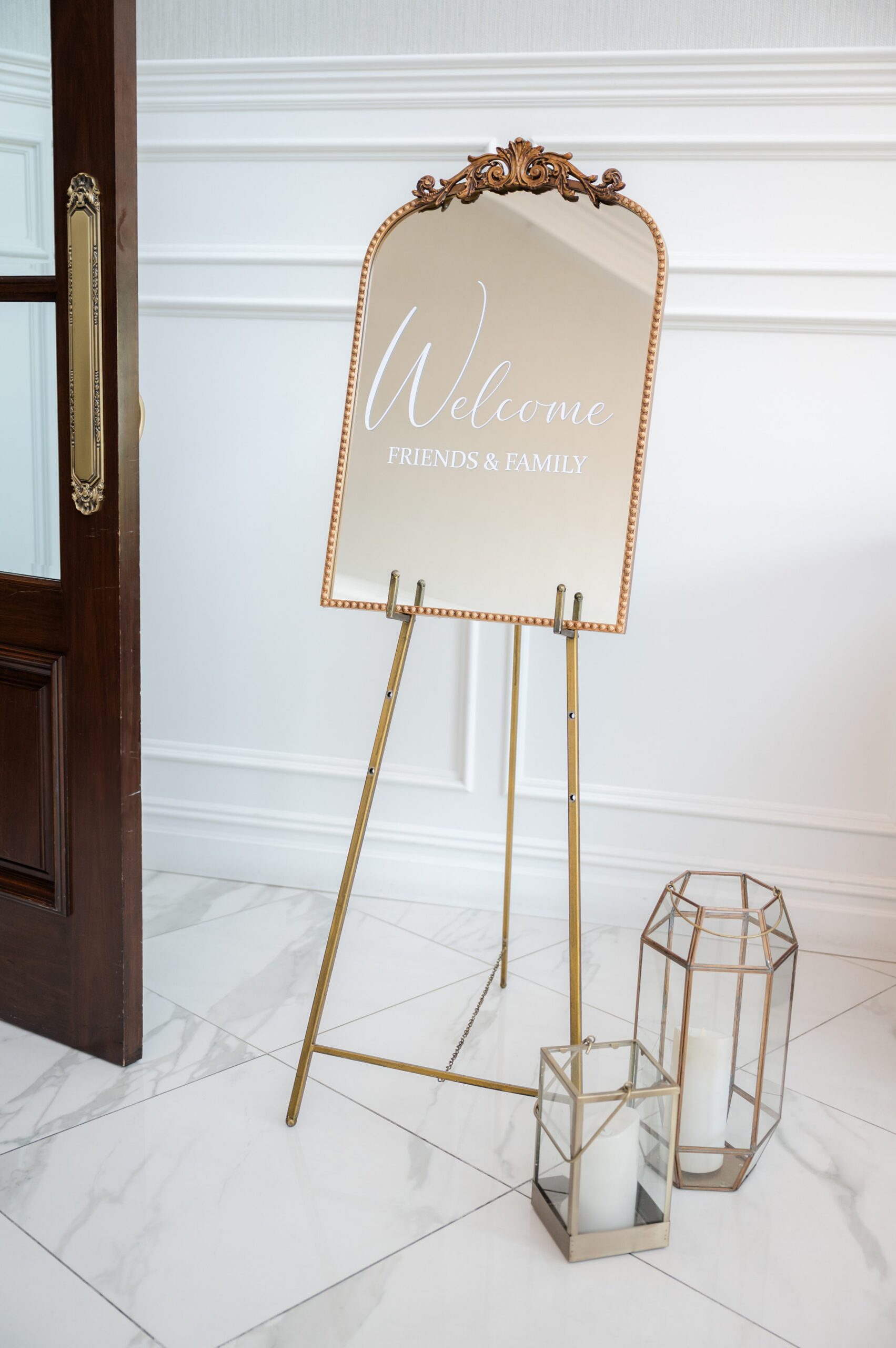 Welcome sign on a gold easel with calligraphy text, displayed indoors beside decorative lanterns and a wooden door