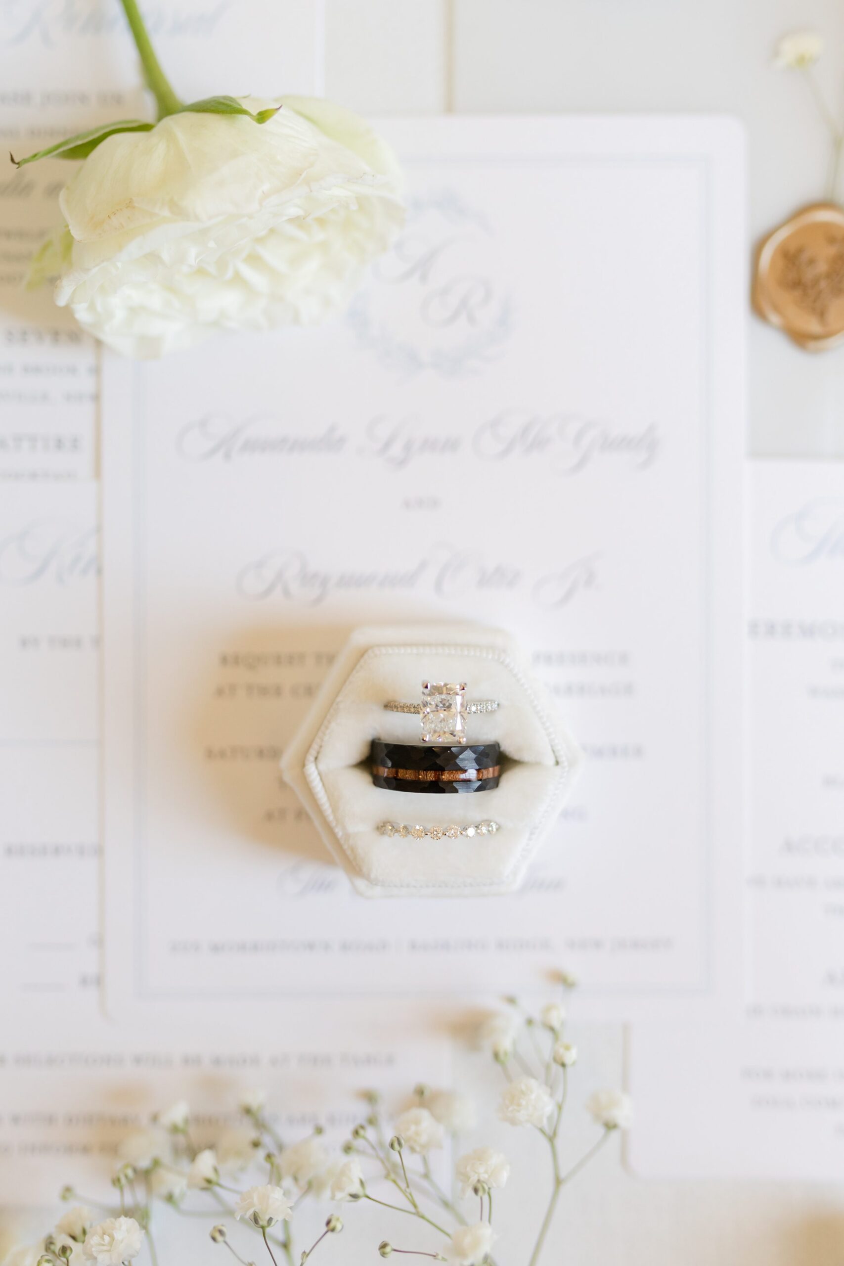 Wedding invitation with a ring in a box, surrounded by soft white flowers on a neutral background
