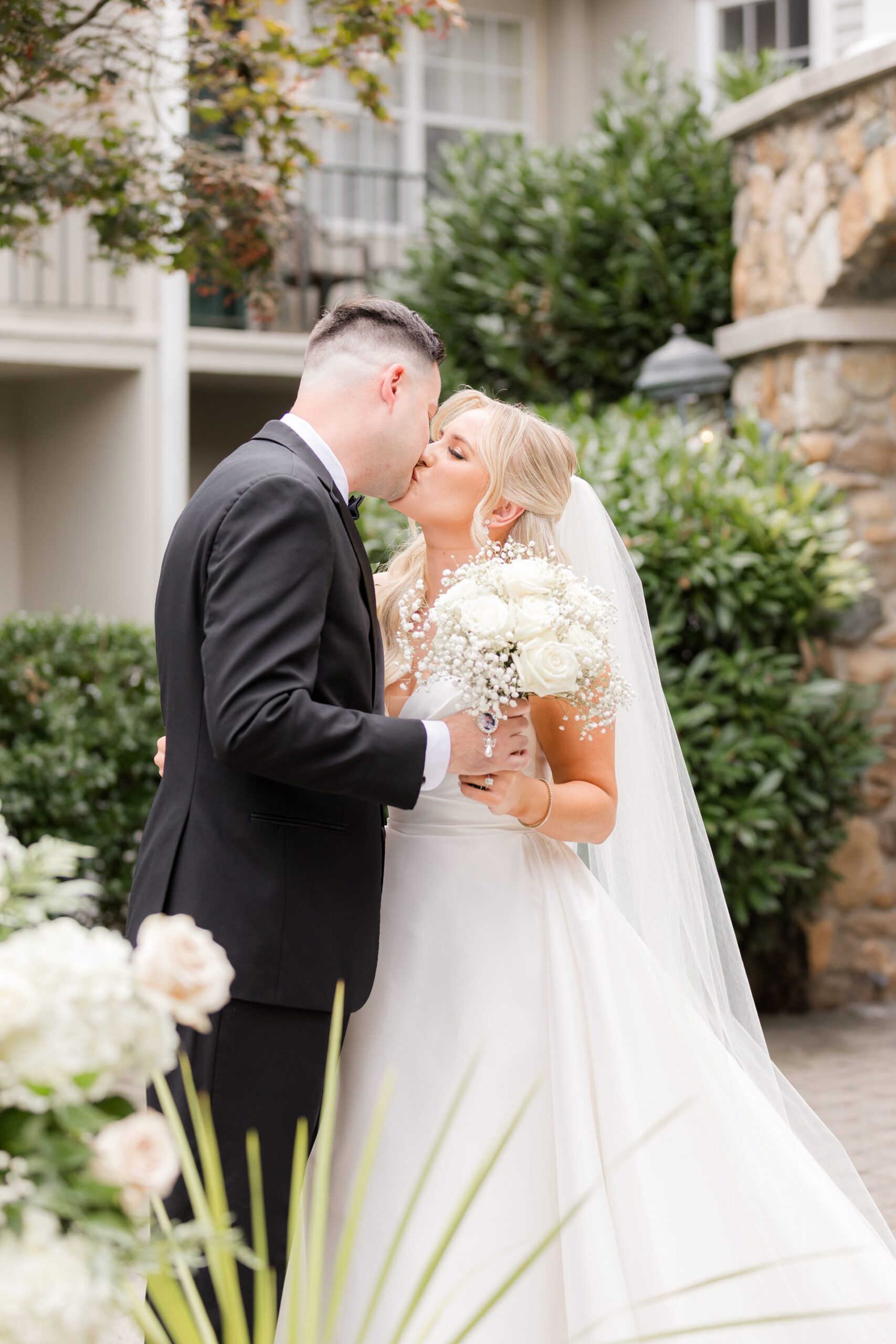 Bride and groom sharing a kiss outdoors, with the bride holding a bouquet