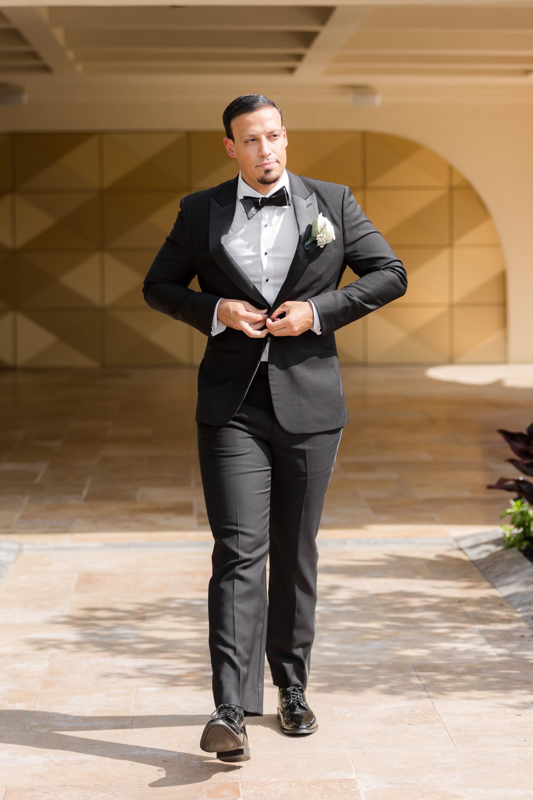 Groom in a black tuxedo walking confidently while adjusting his jacket