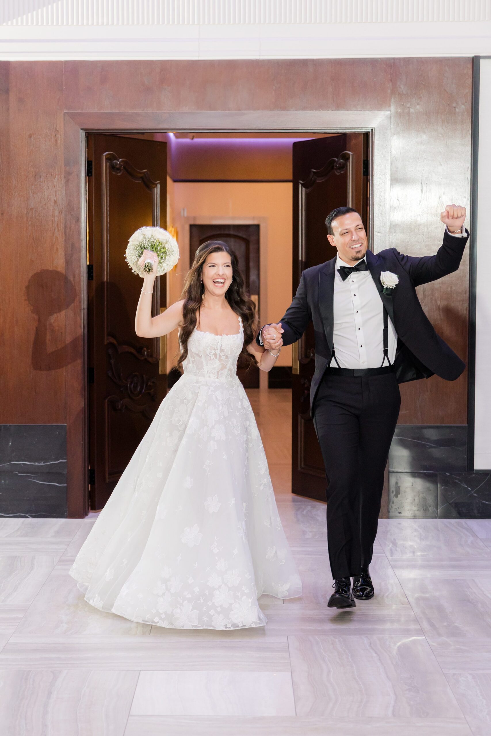 Bride and groom make a lively entrance, raising their hands and celebrating as they step into the reception