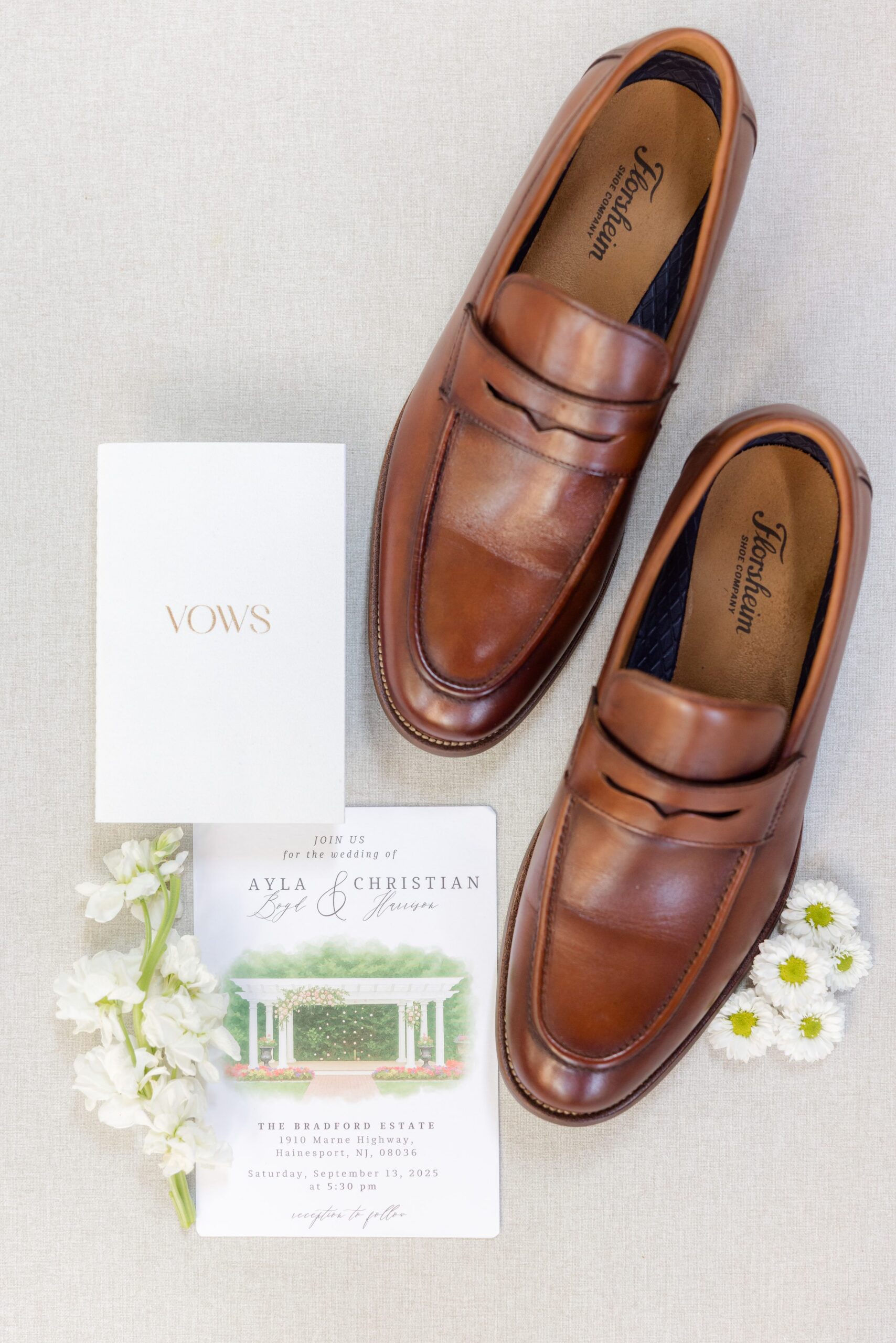 Brown leather groom’s shoes styled with wedding stationery and soft florals