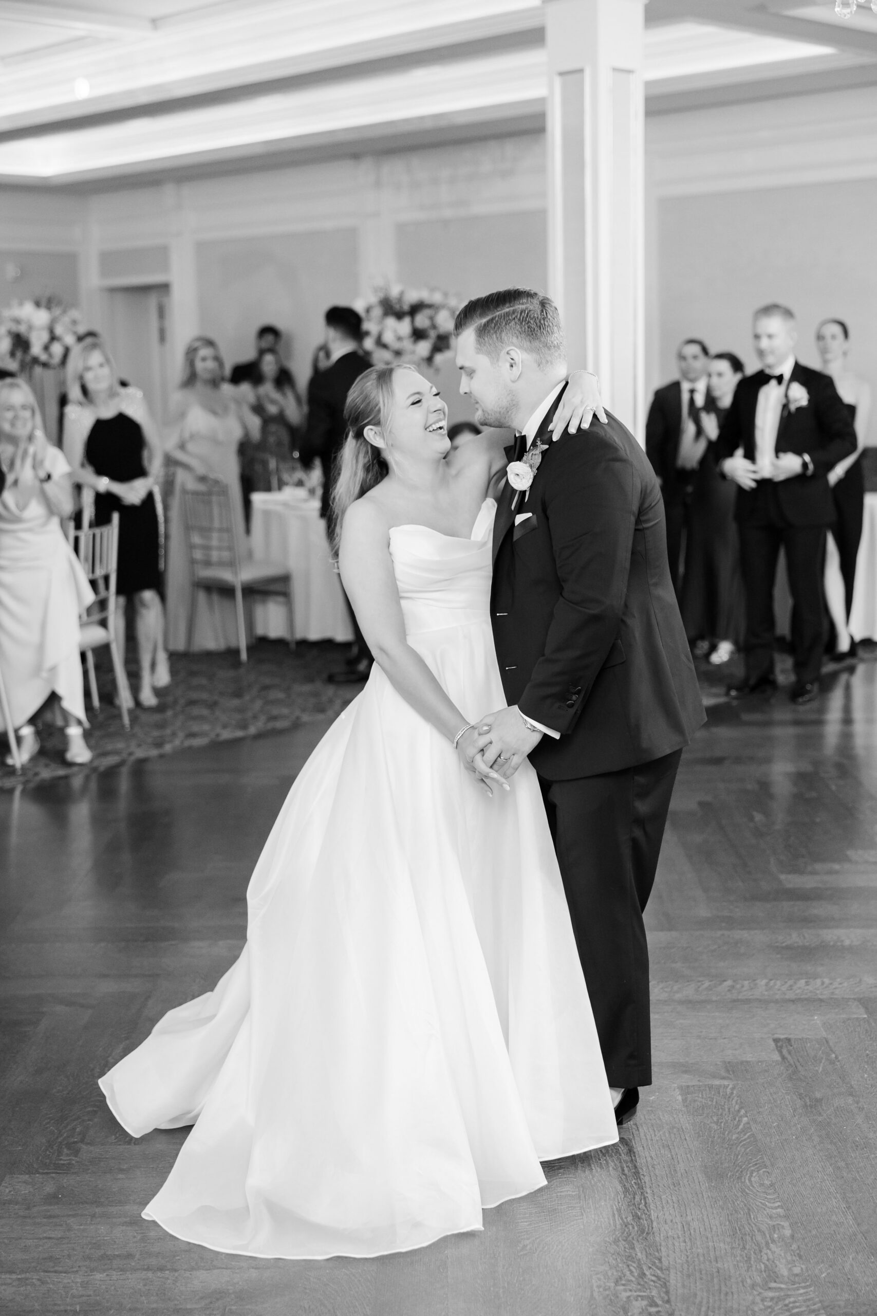 Bride and groom sharing their first dance, holding each other close while guests look on, capturing a heartfelt and intimate moment