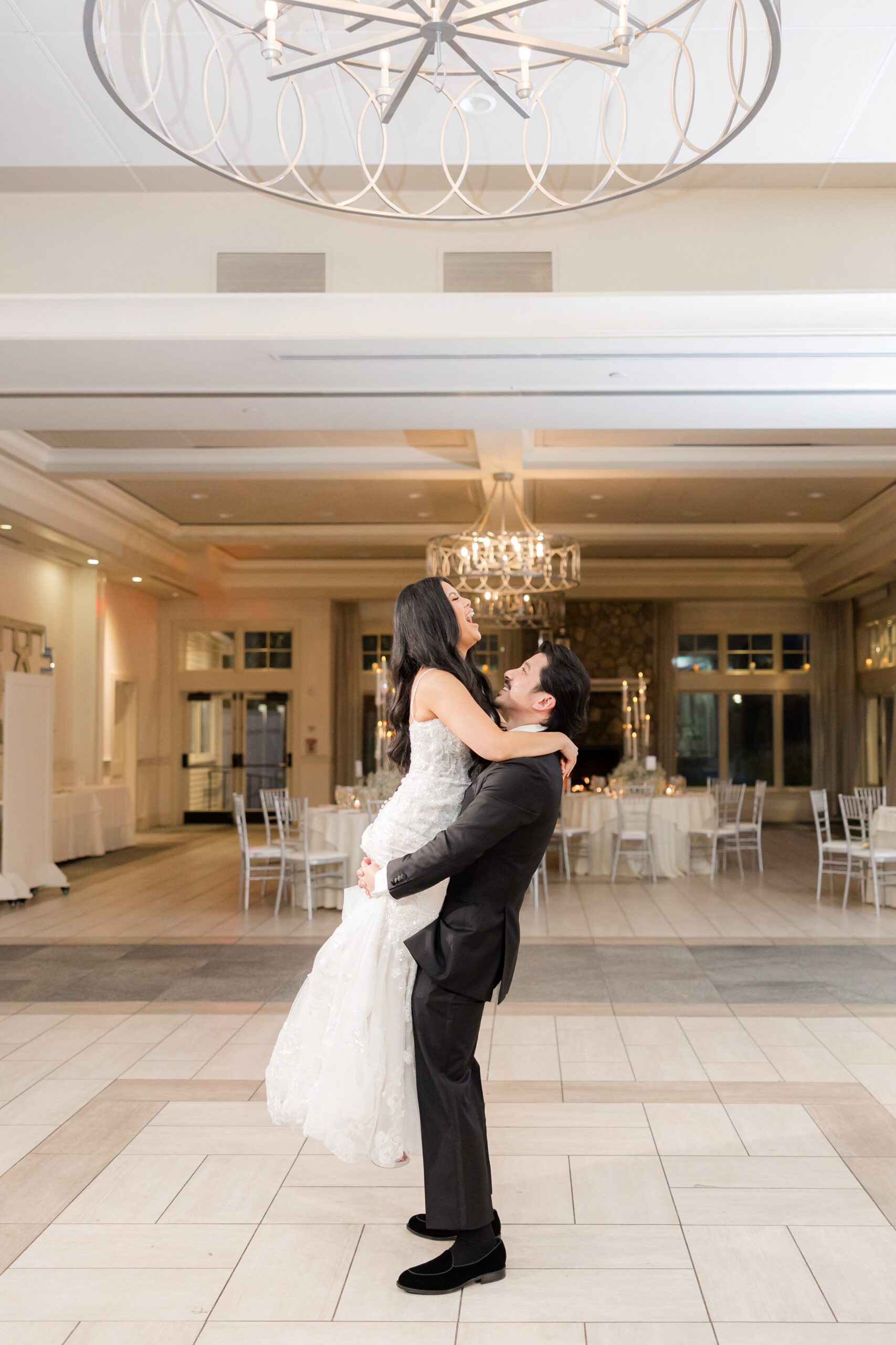 Groom lifts his bride joyfully, their laughter and love filling the grand, light-filled room