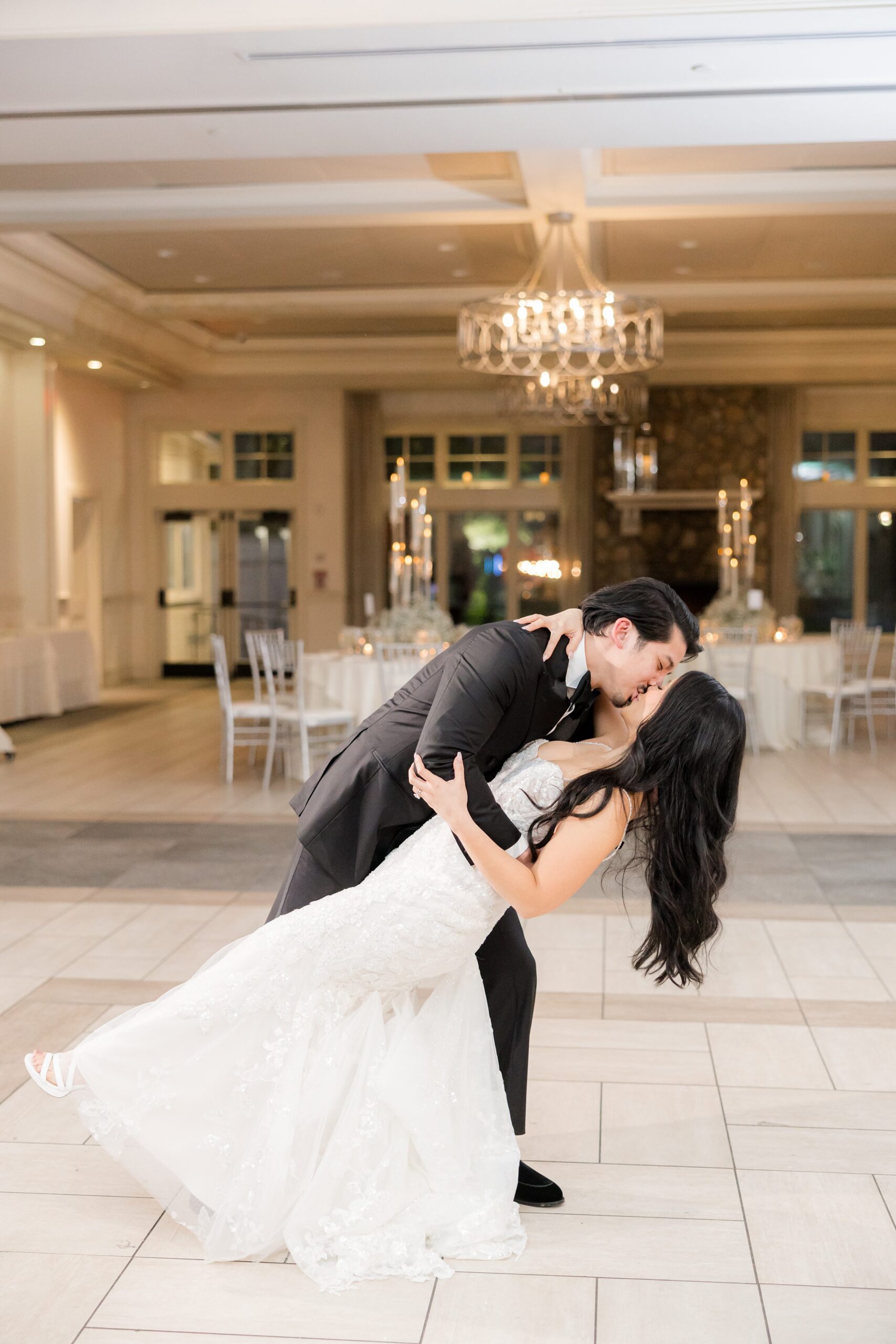 Groom dips his bride in a sweeping, cinematic moment beneath a glowing chandelier, capturing pure romance