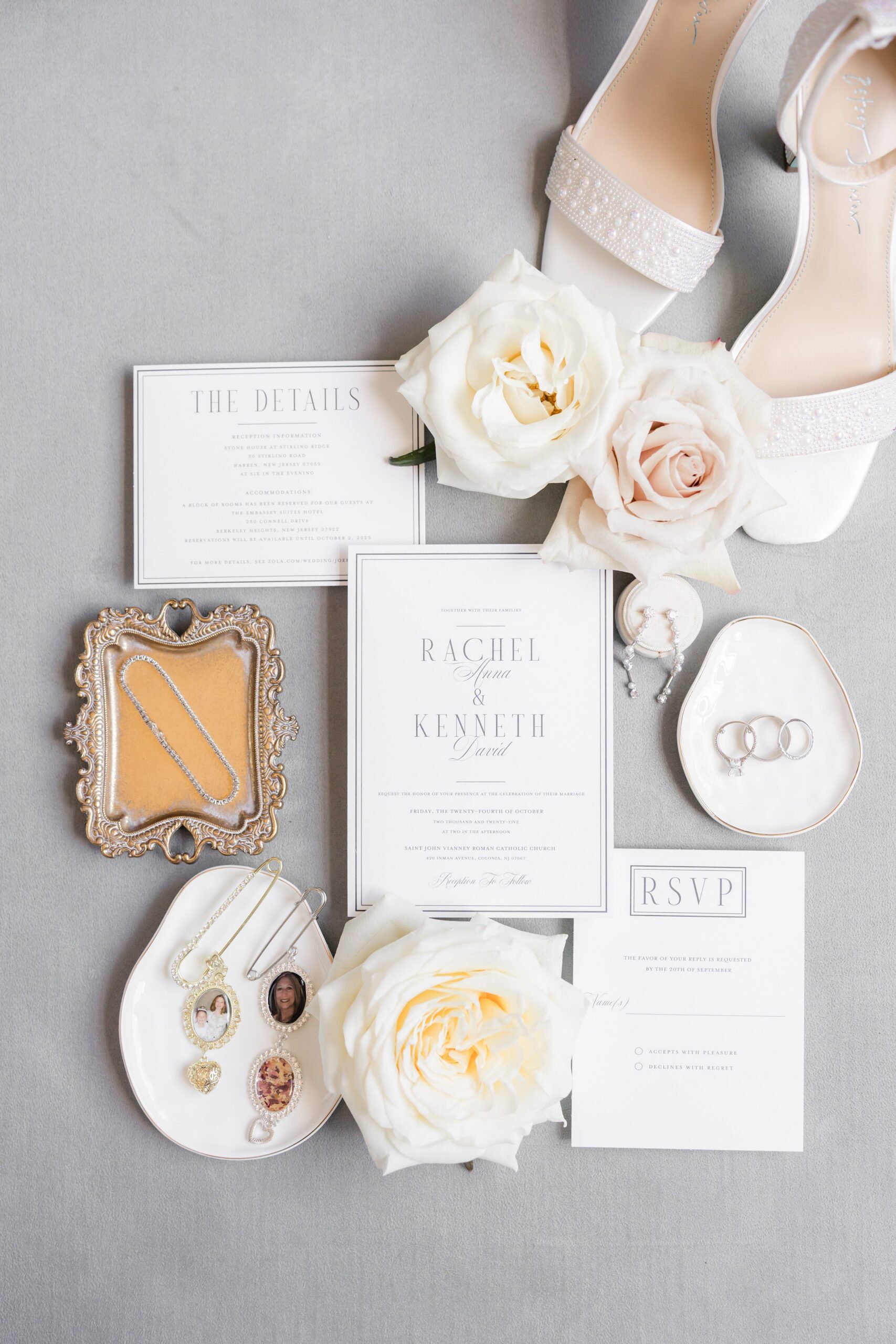 Wedding stationery flat lay with roses, white heels, perfume, jewelry, and neutral-toned invitation cards on a gray background