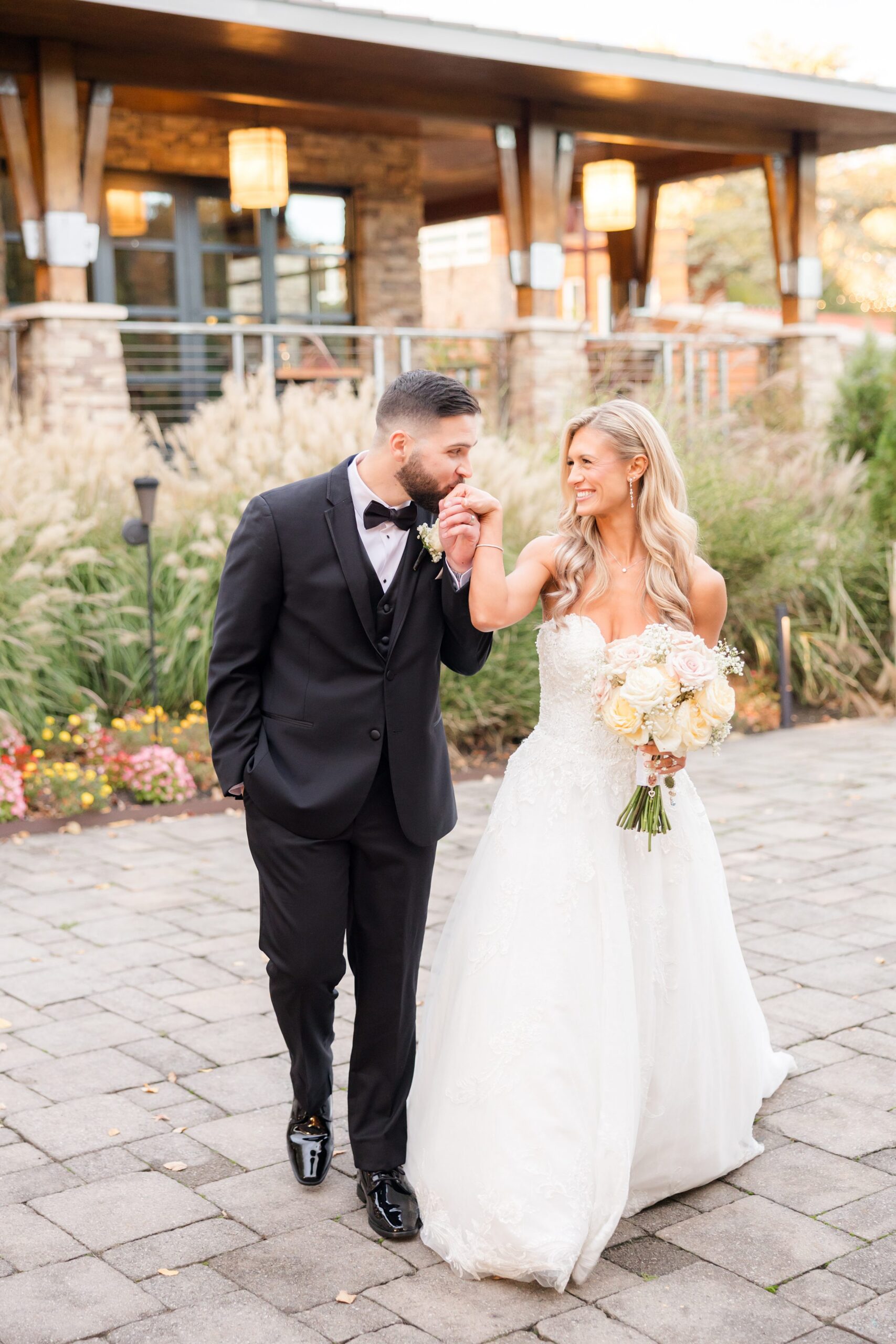 Bride and groom walking together outdoors, smiling at each other as the bride holds her bouquet, capturing a joyful and relaxed newlywed moment