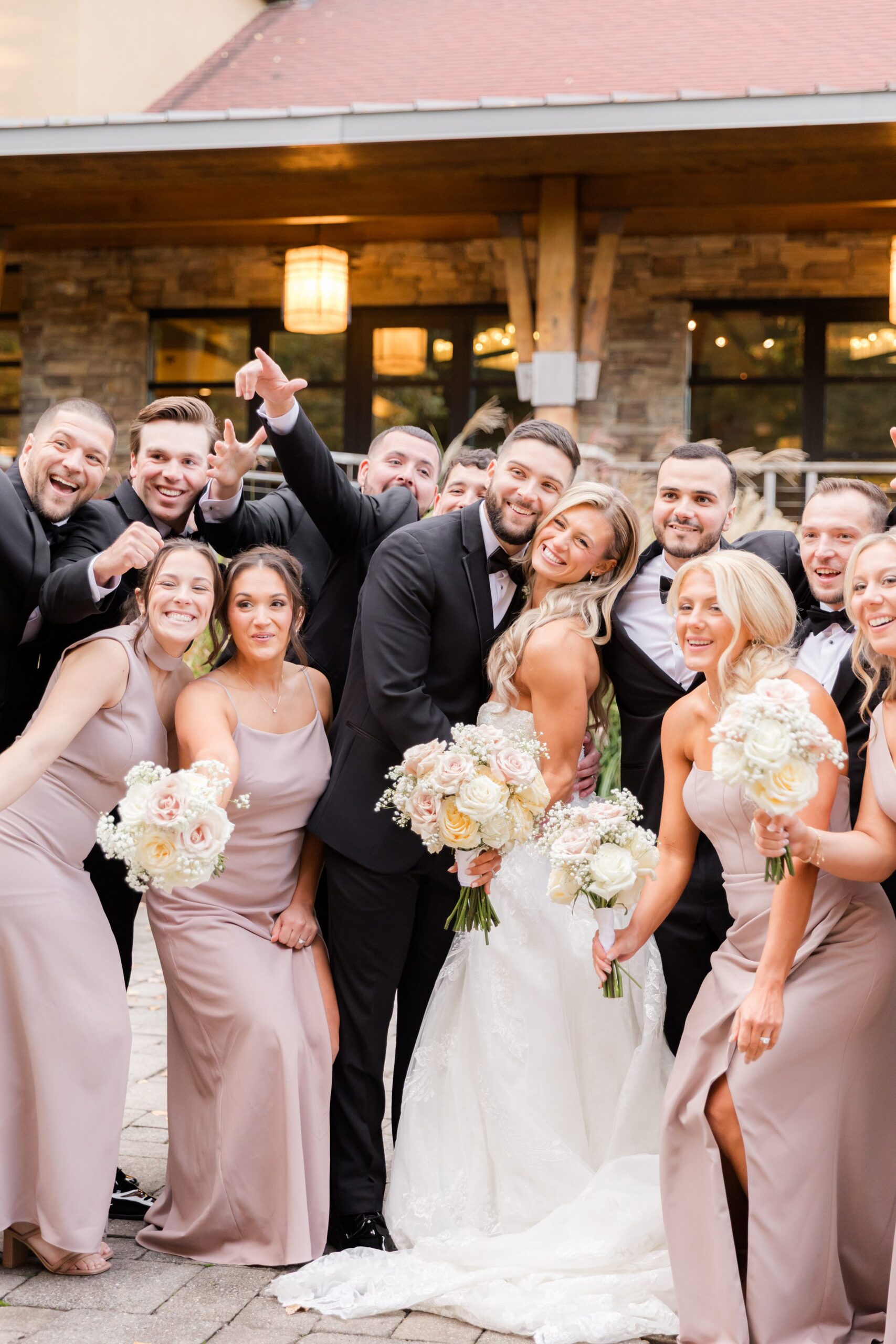 Bride and groom surrounded by bridesmaids and groomsmen, smiling and posing together while holding bouquets in a joyful group wedding photo