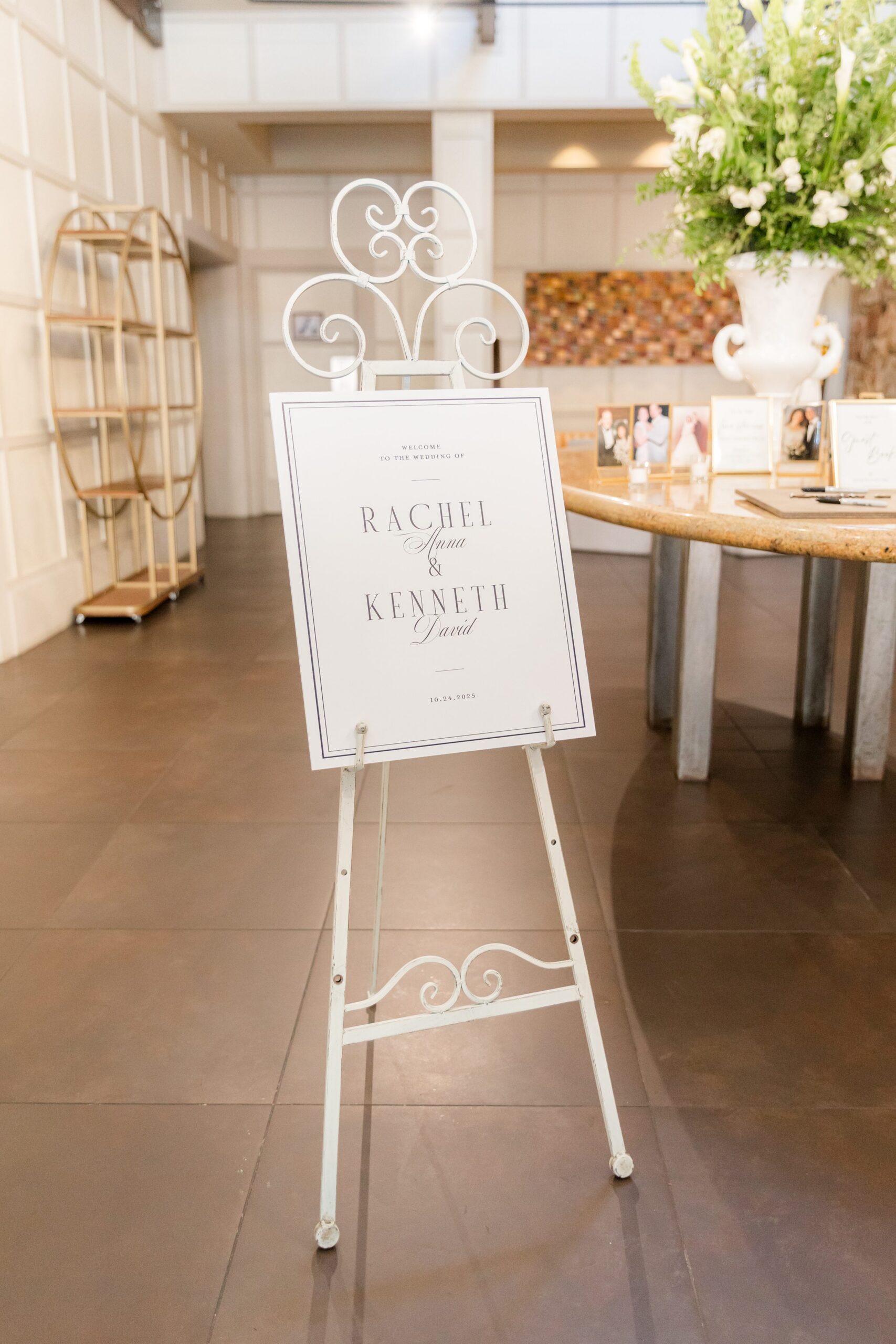 Elegant white welcome sign on a decorative easel stands at the entrance of a wedding venue, surrounded by soft lighting and floral arrangements, creating a warm and inviting atmosphere