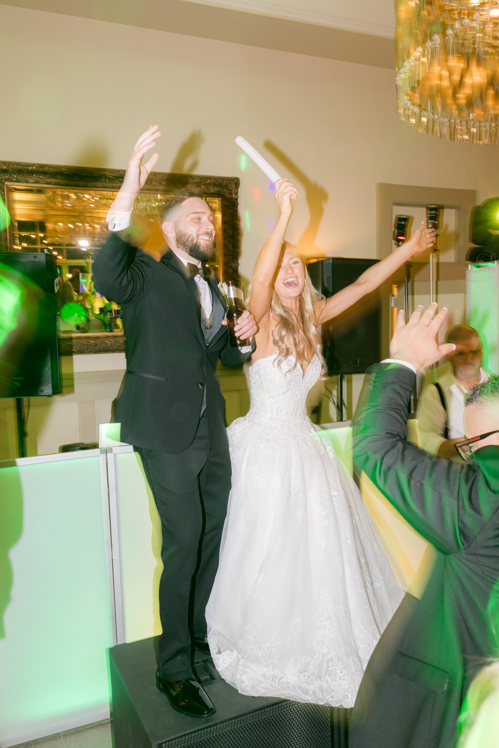 Bride and groom standing on a platform with hands raised, celebrating and dancing as guests cheer around them