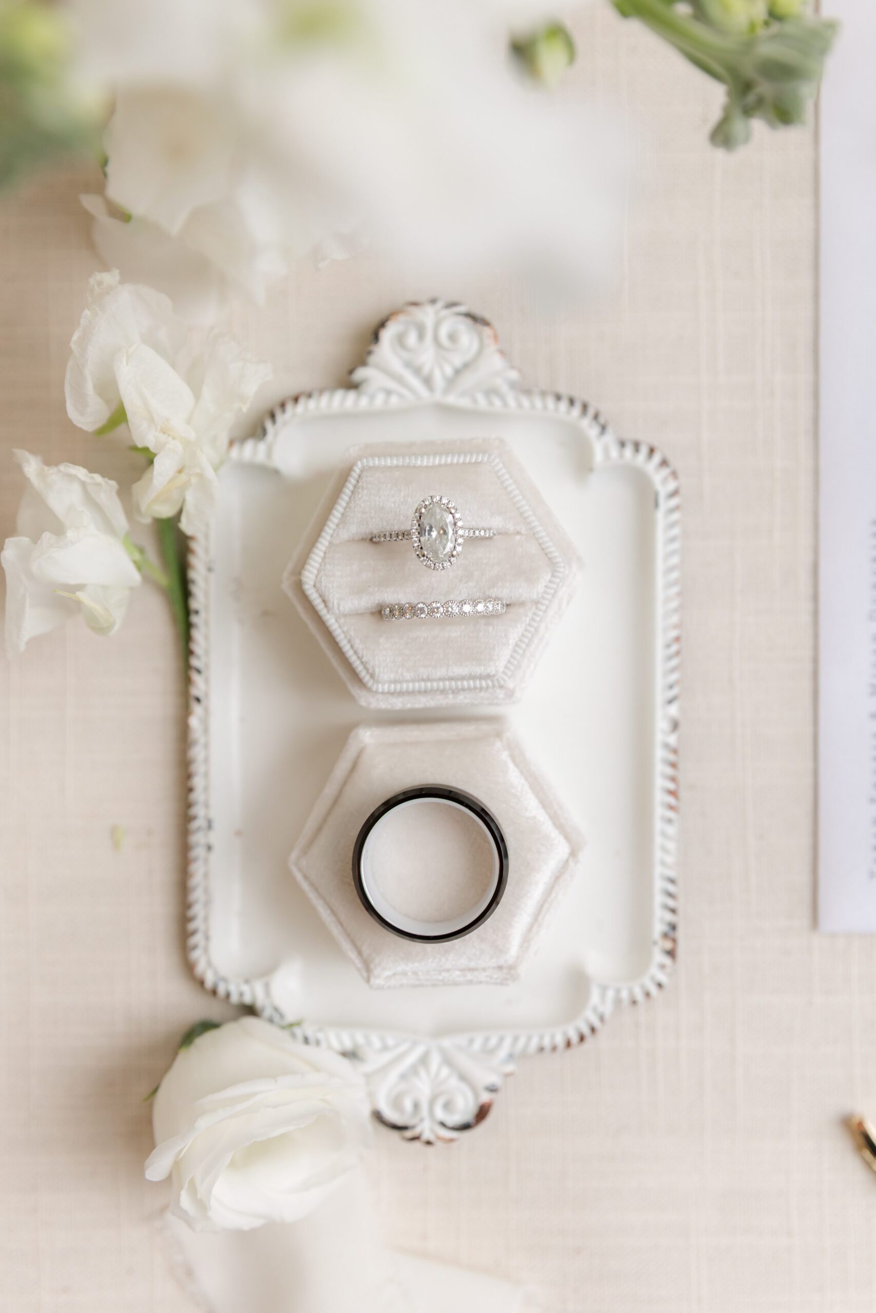Wedding ring set displayed in an elegant ring box on a decorative tray, surrounded by soft white florals