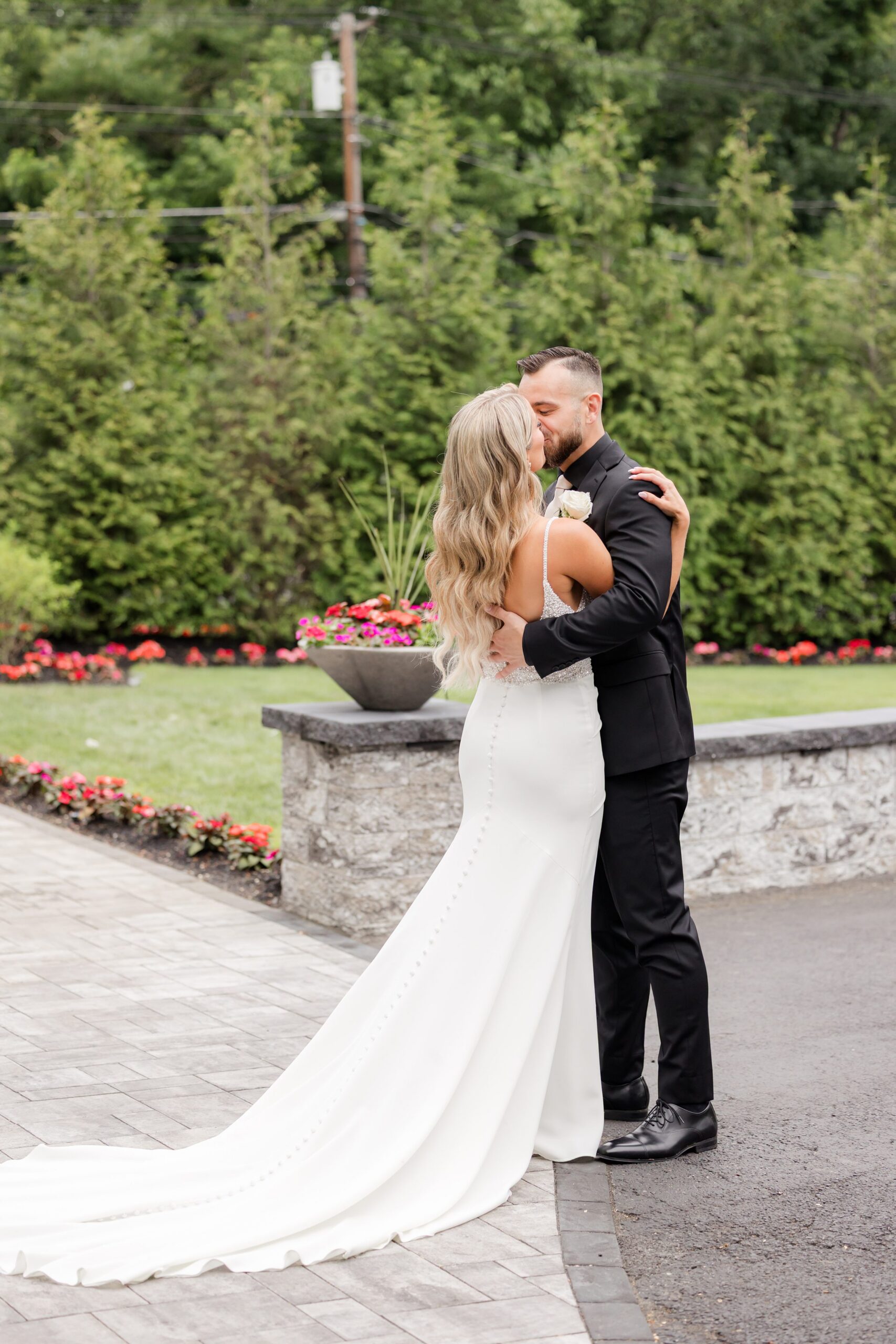 Bride and groom sharing a romantic kiss outdoors, embracing closely with her gown flowing behind her in a serene garden setting