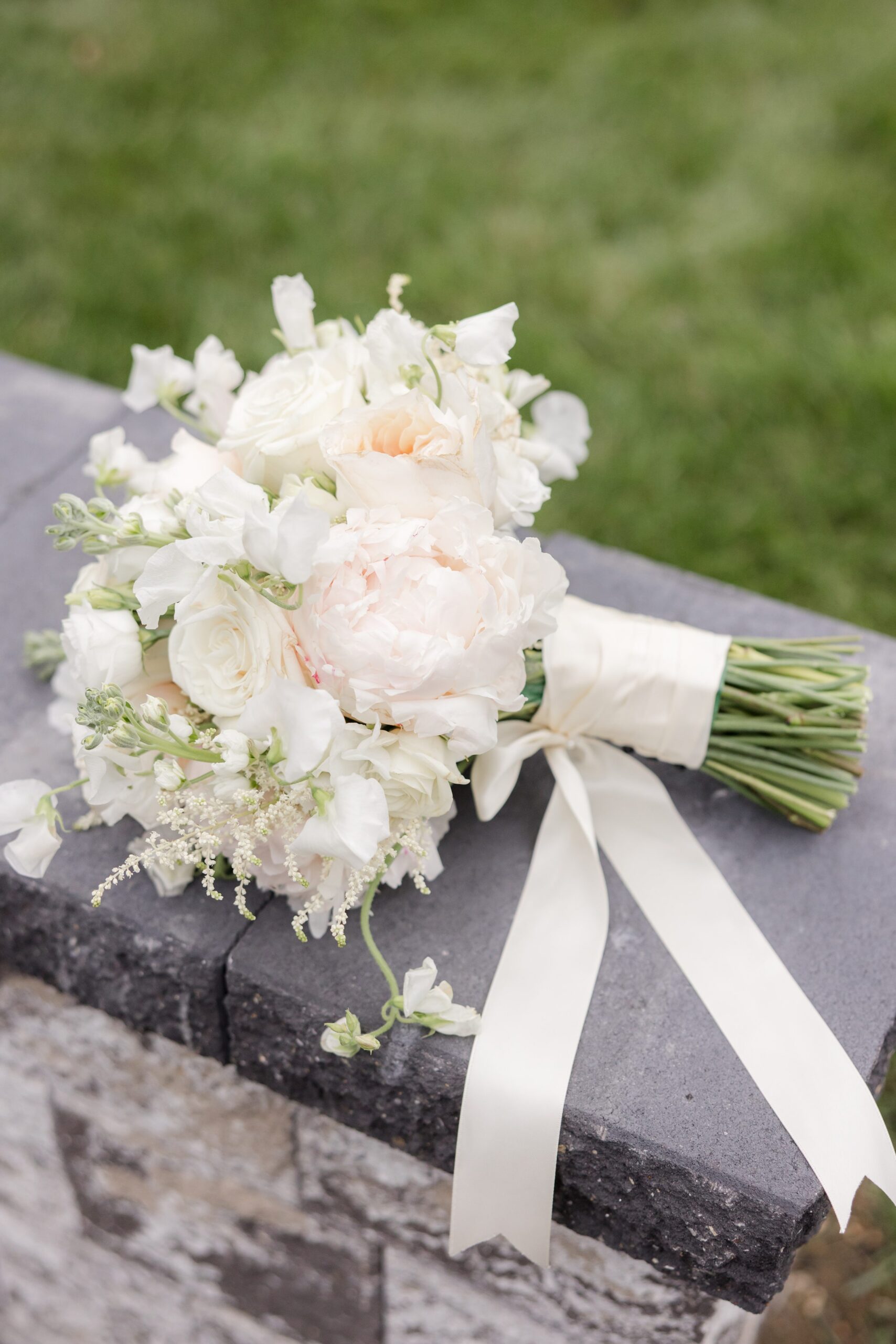 Bridal bouquet of white flowers with soft greenery, tied with a flowing ribbon and resting on a stone ledge