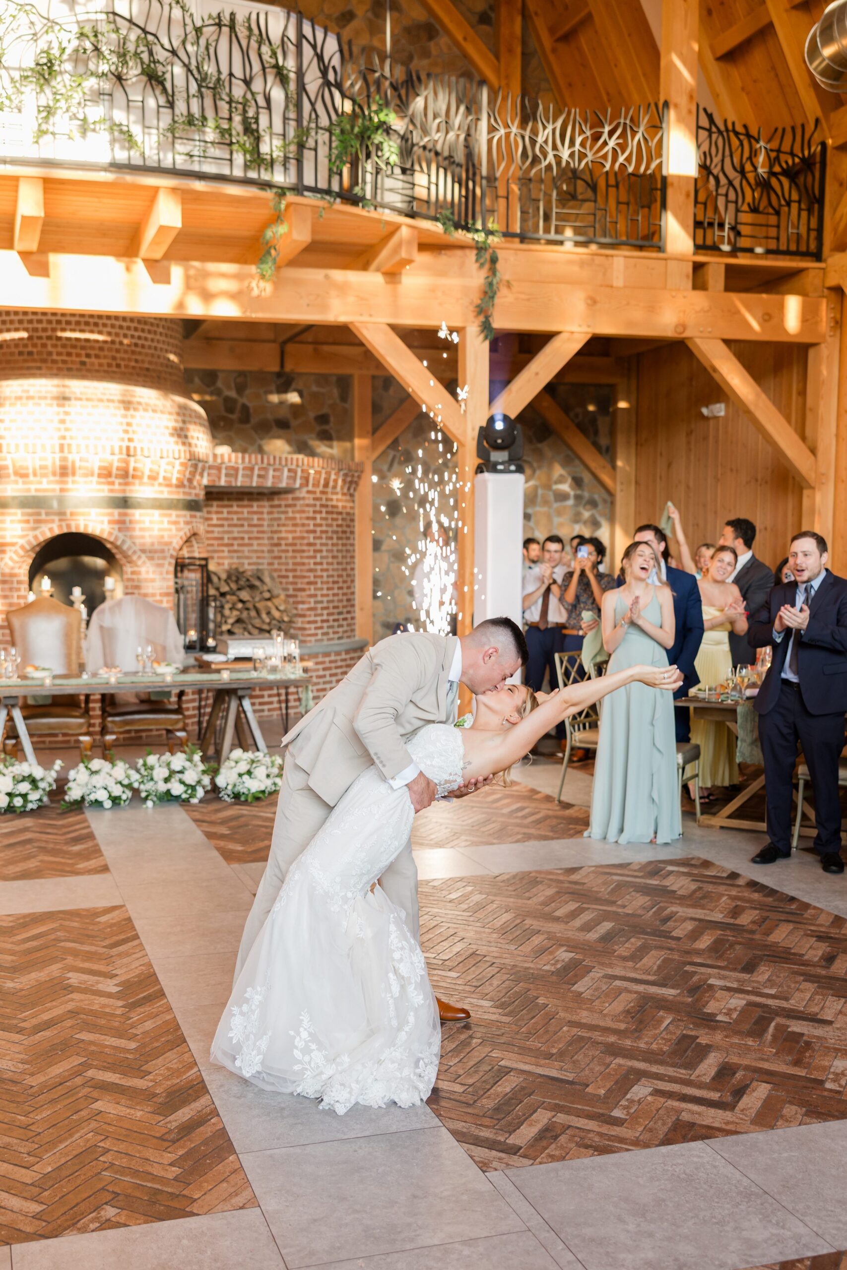 Bride and groom sharing a playful kiss as they celebrate on the dance floor, with guests smiling and cheering in the background