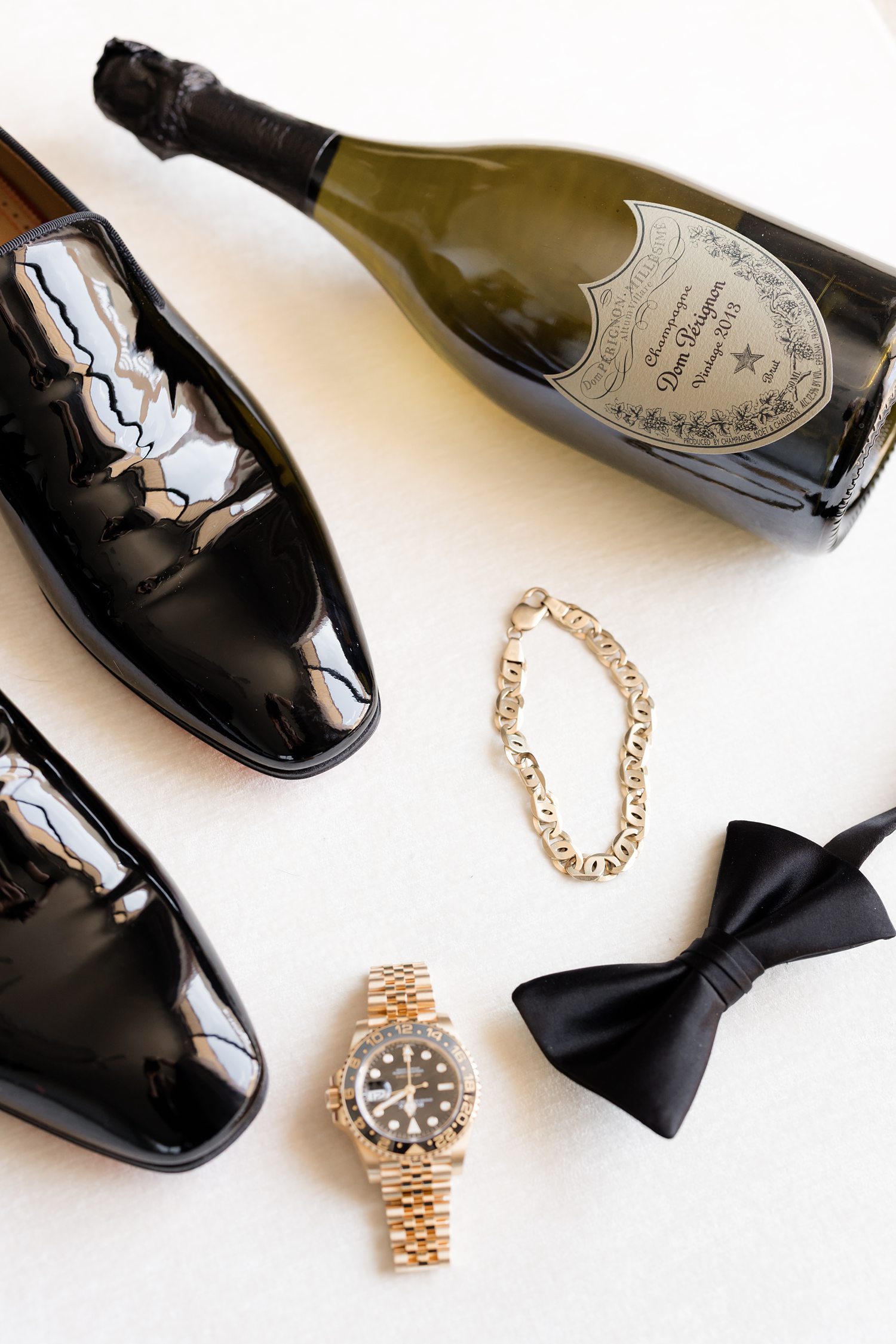 Groom accessories flat lay with champagne, cufflinks, and tuxedo details