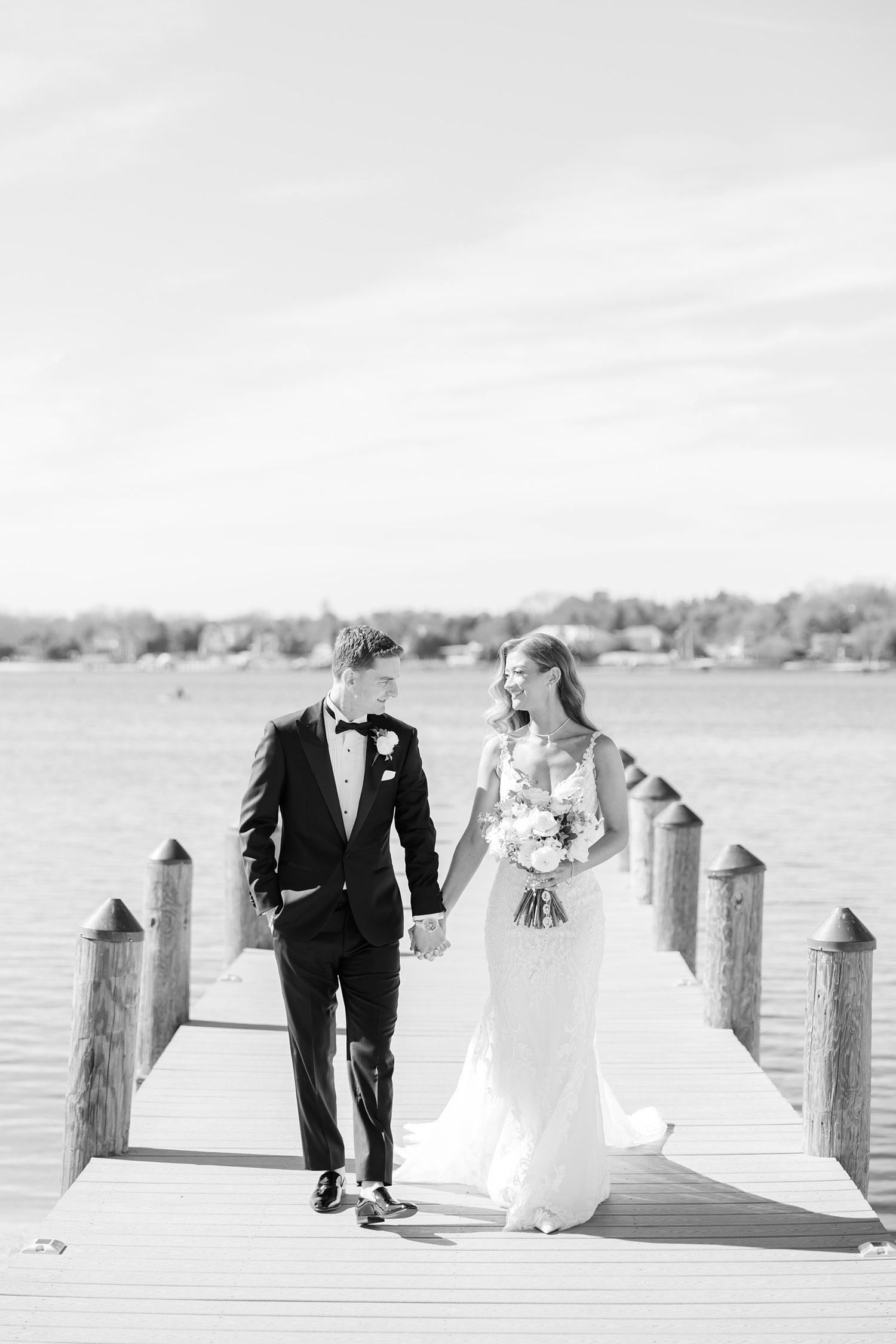 Black and white photo of bride and groom walking along marina pier
