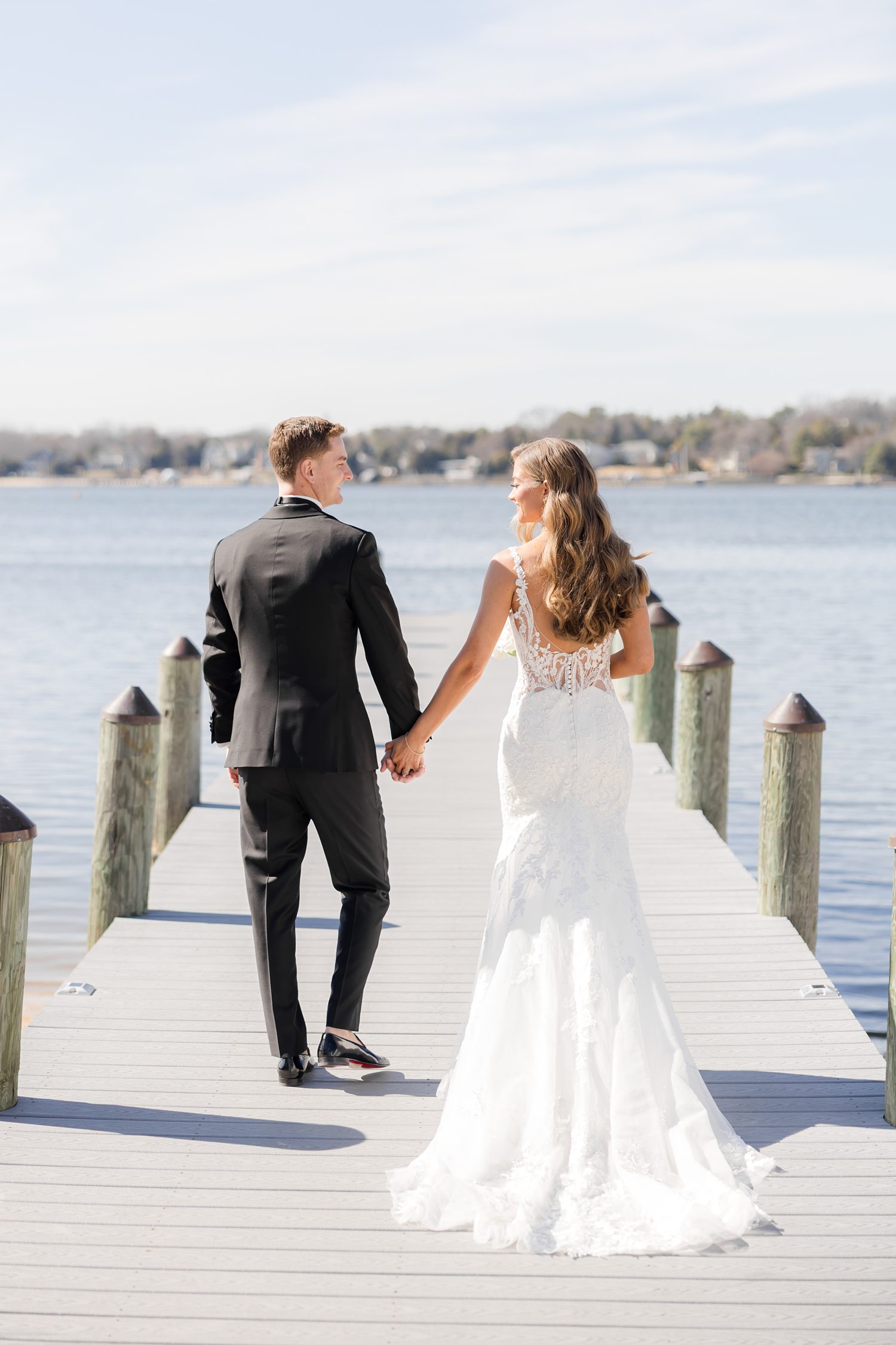 Bride and groom holding hands beside waterfront during elegant wedding portraits