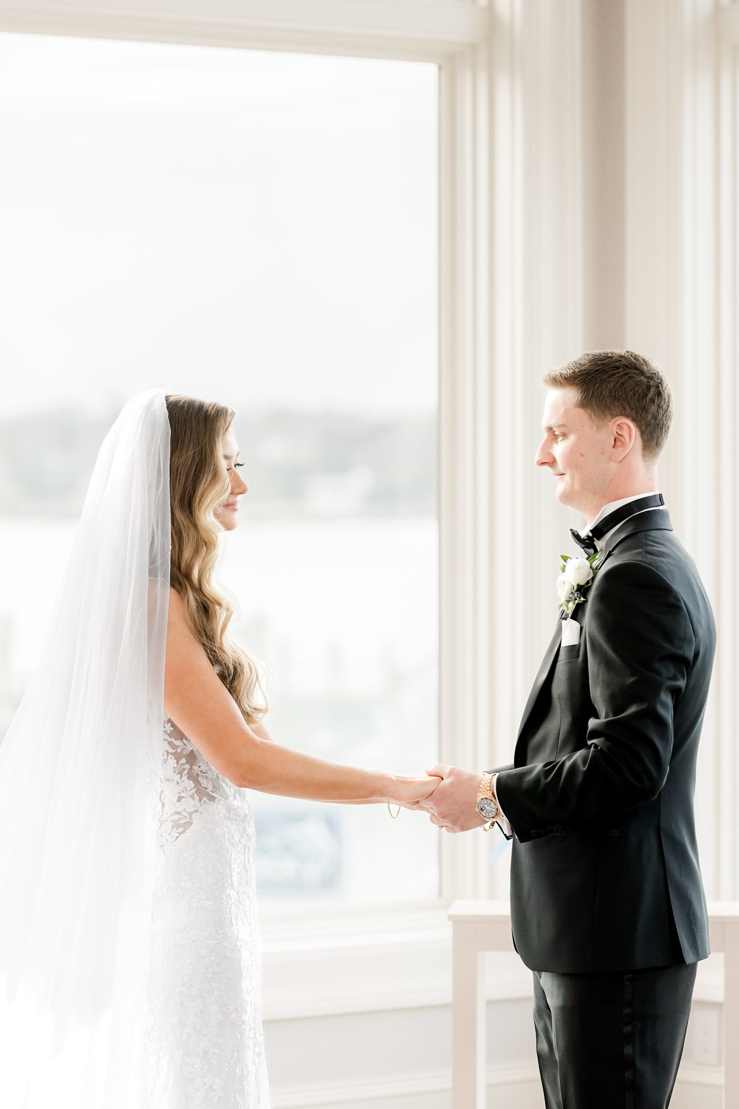 Bride and groom sharing emotional first look by bright ballroom window