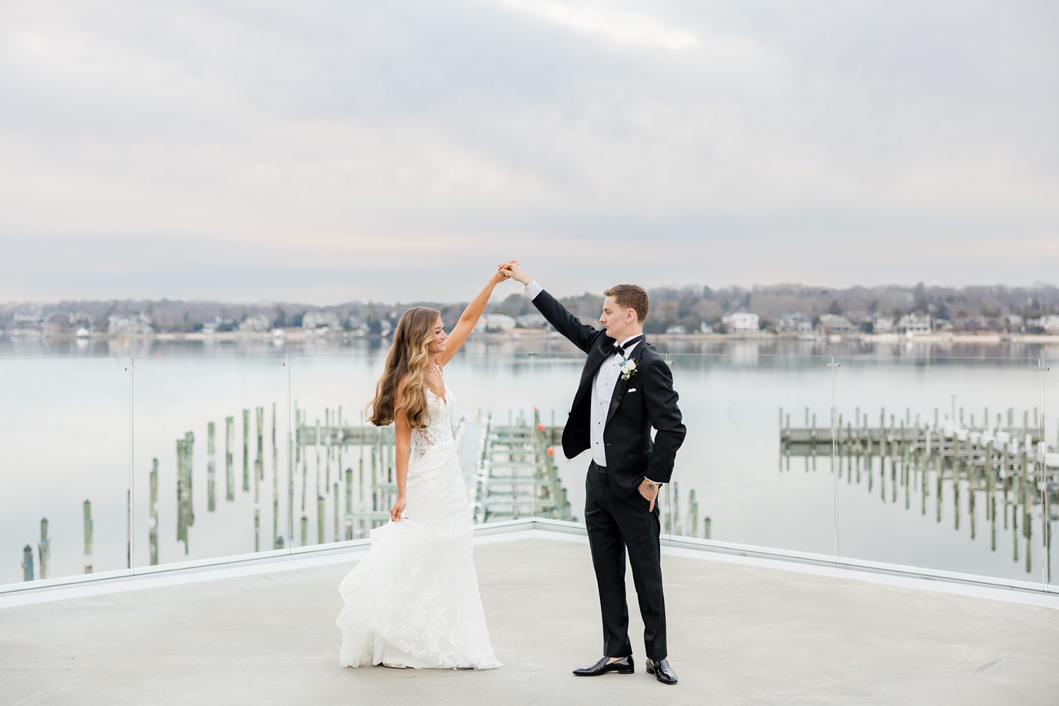 Bride and groom embracing on waterfront balcony during romantic wedding portraits