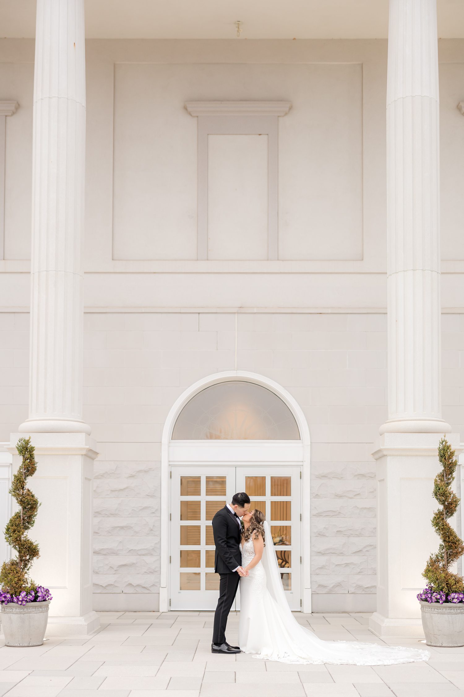 Bride and groom embracing in front of elegant white wedding venue